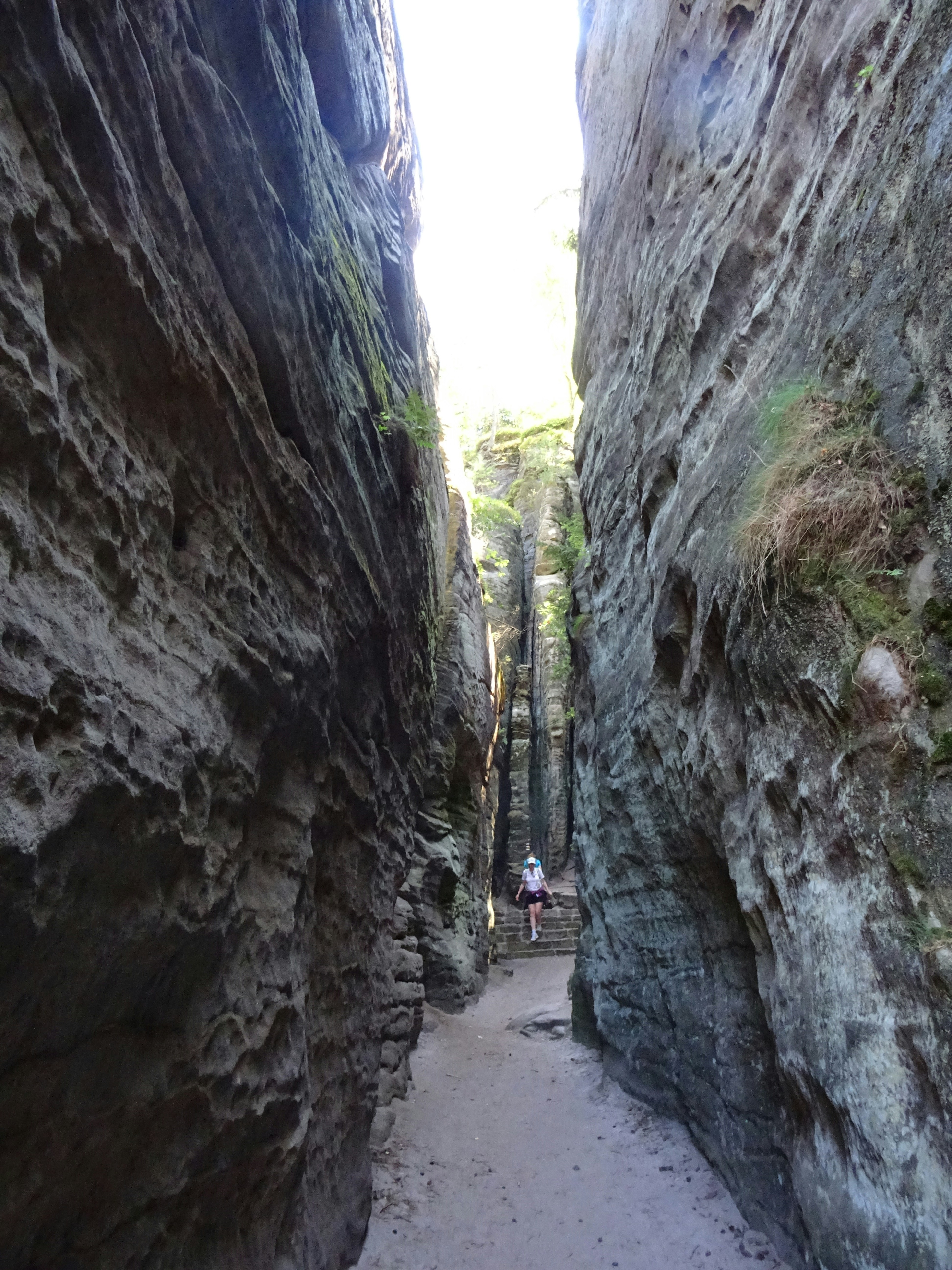 A person walking through a narrow sandstone gorge with high vertical rock walls