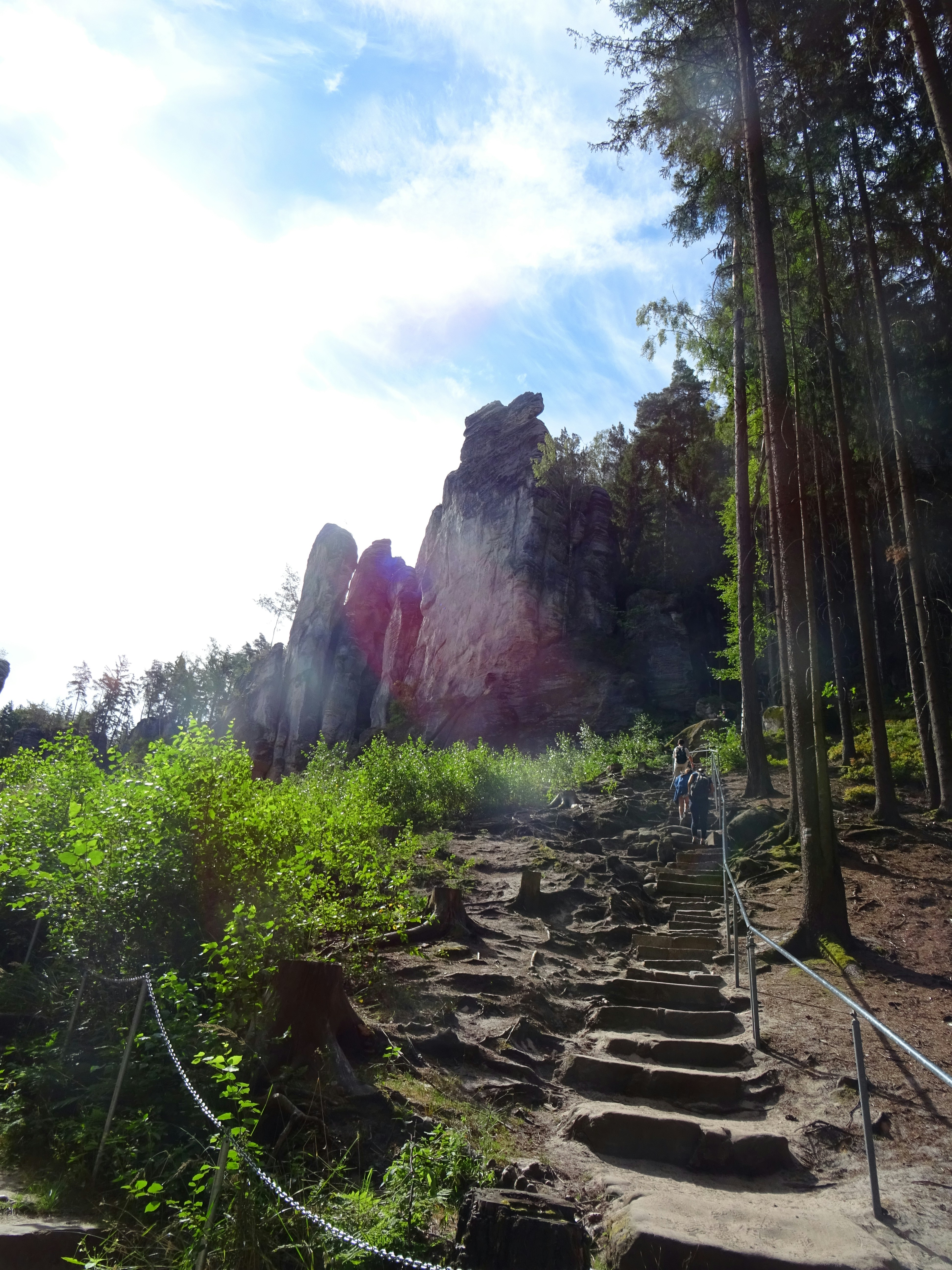 People climbing stone stairs toward tall sandstone rock formations in a forest
