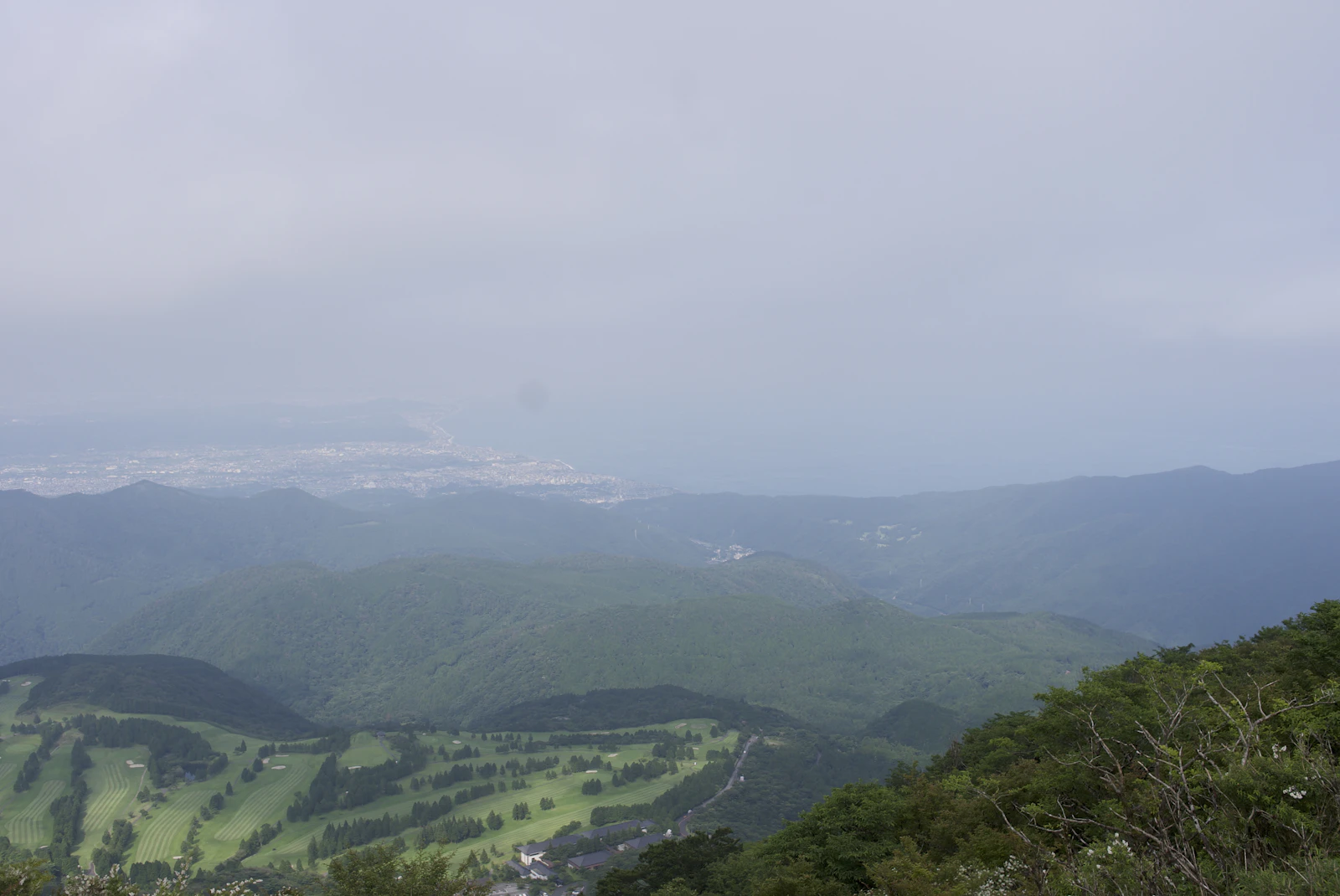 A golf course on a green hillside near Hakone, Japan, with mountains and a distant town behind
