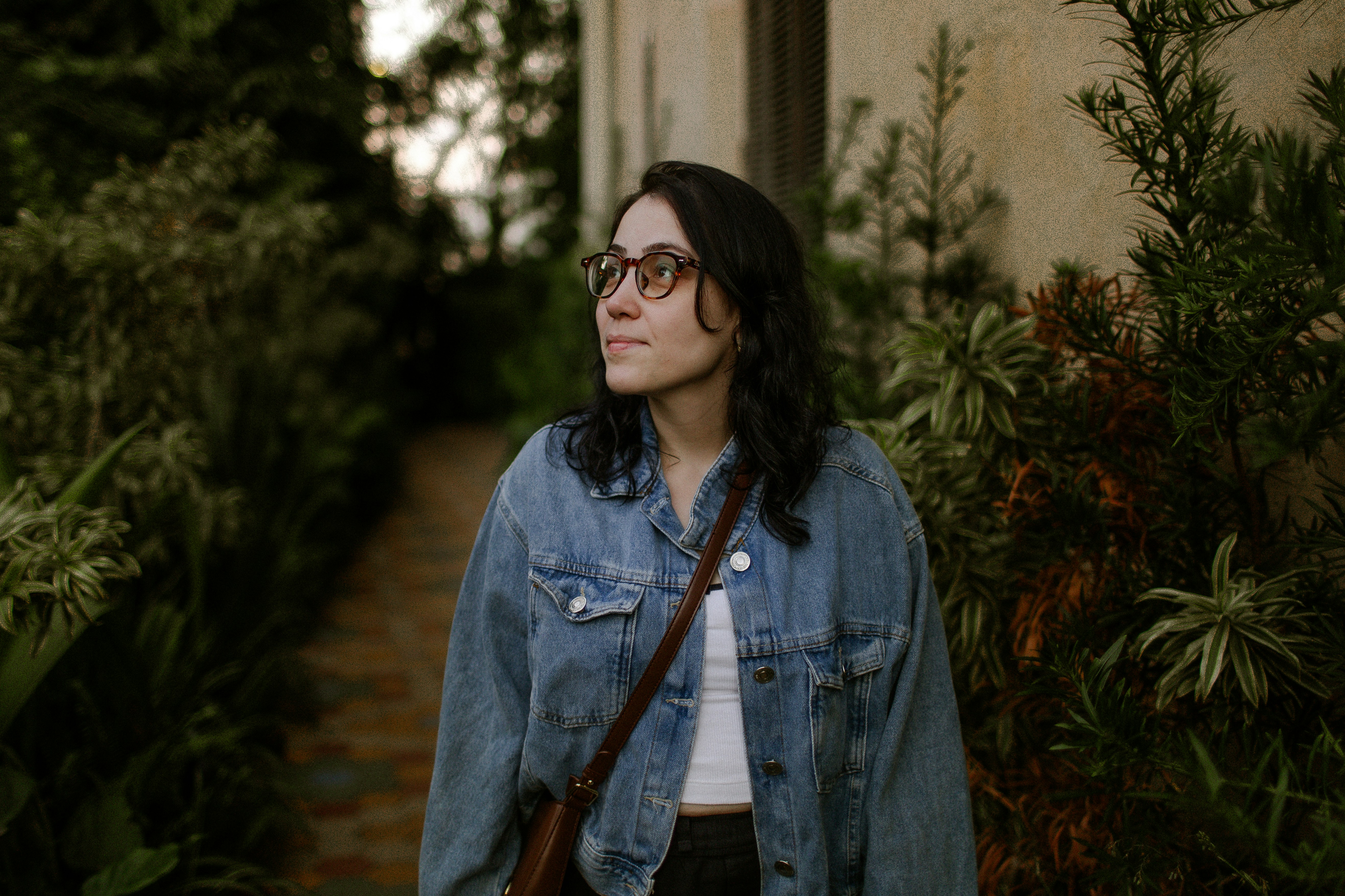 A woman with glasses and a denim jacket in a lush garden path