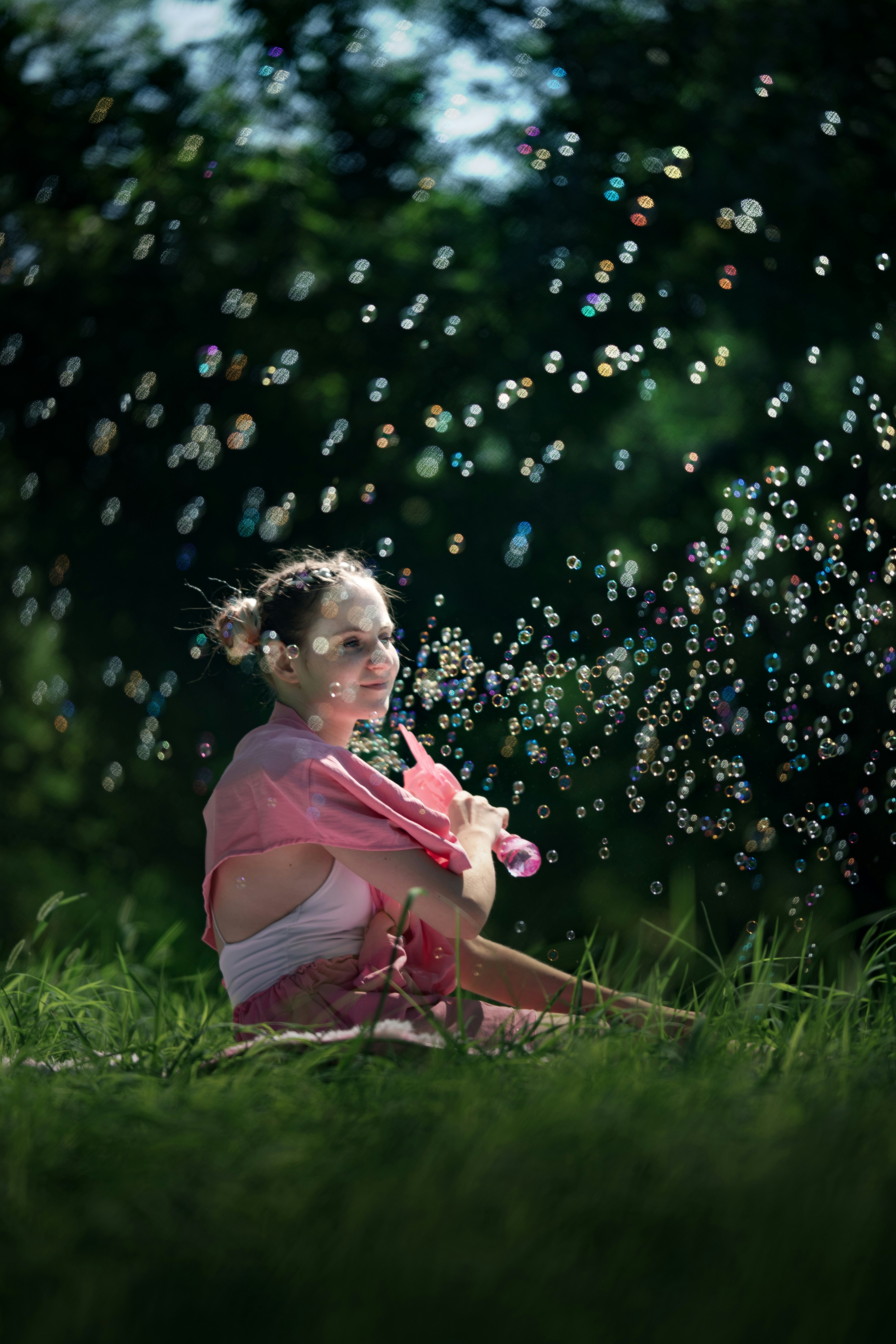 Une femme en chemise rose soufflant des bulles dans un parc herbeux