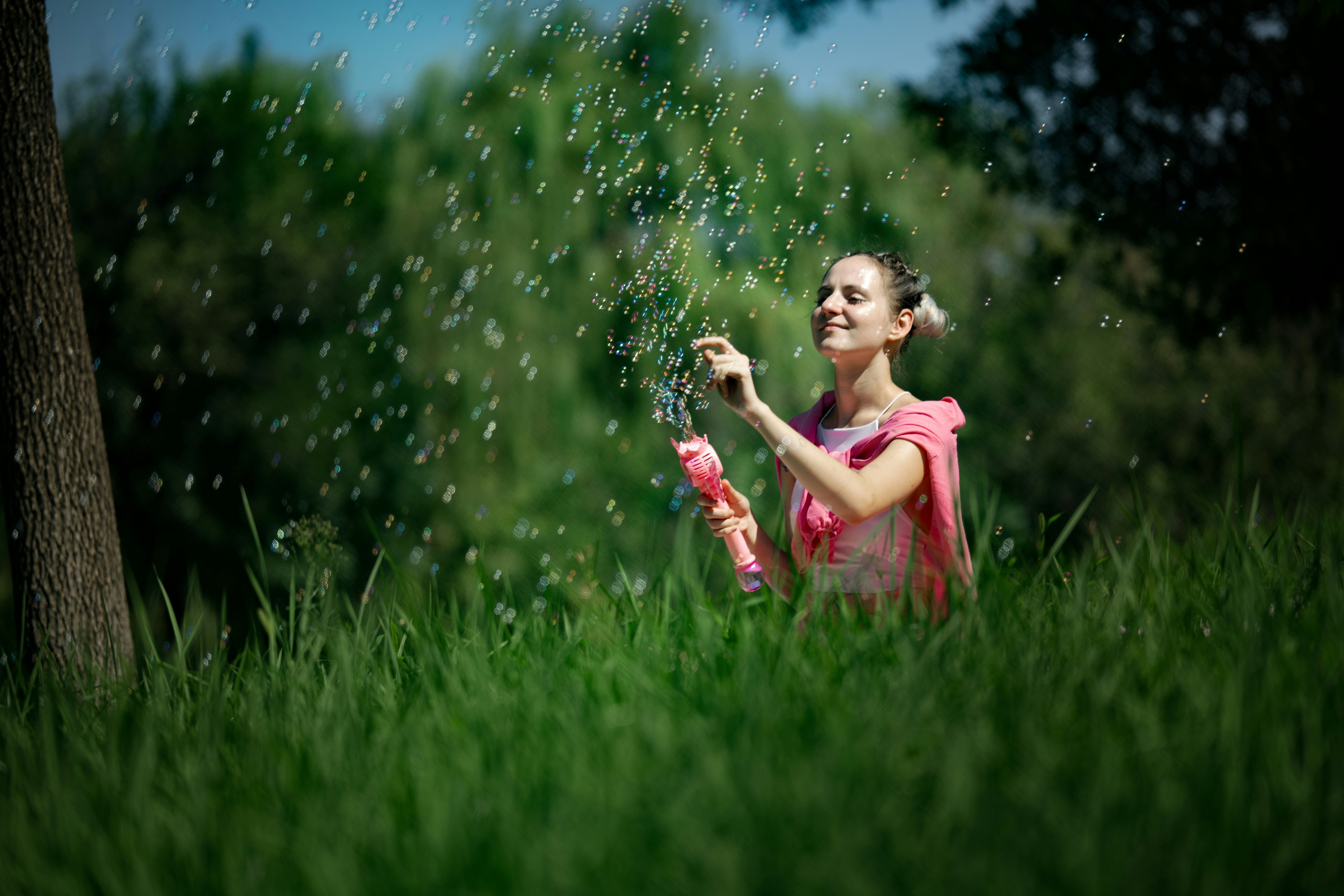 Une femme soufflant des bulles avec une baguette rose dans un parc herbeux baigné de soleil