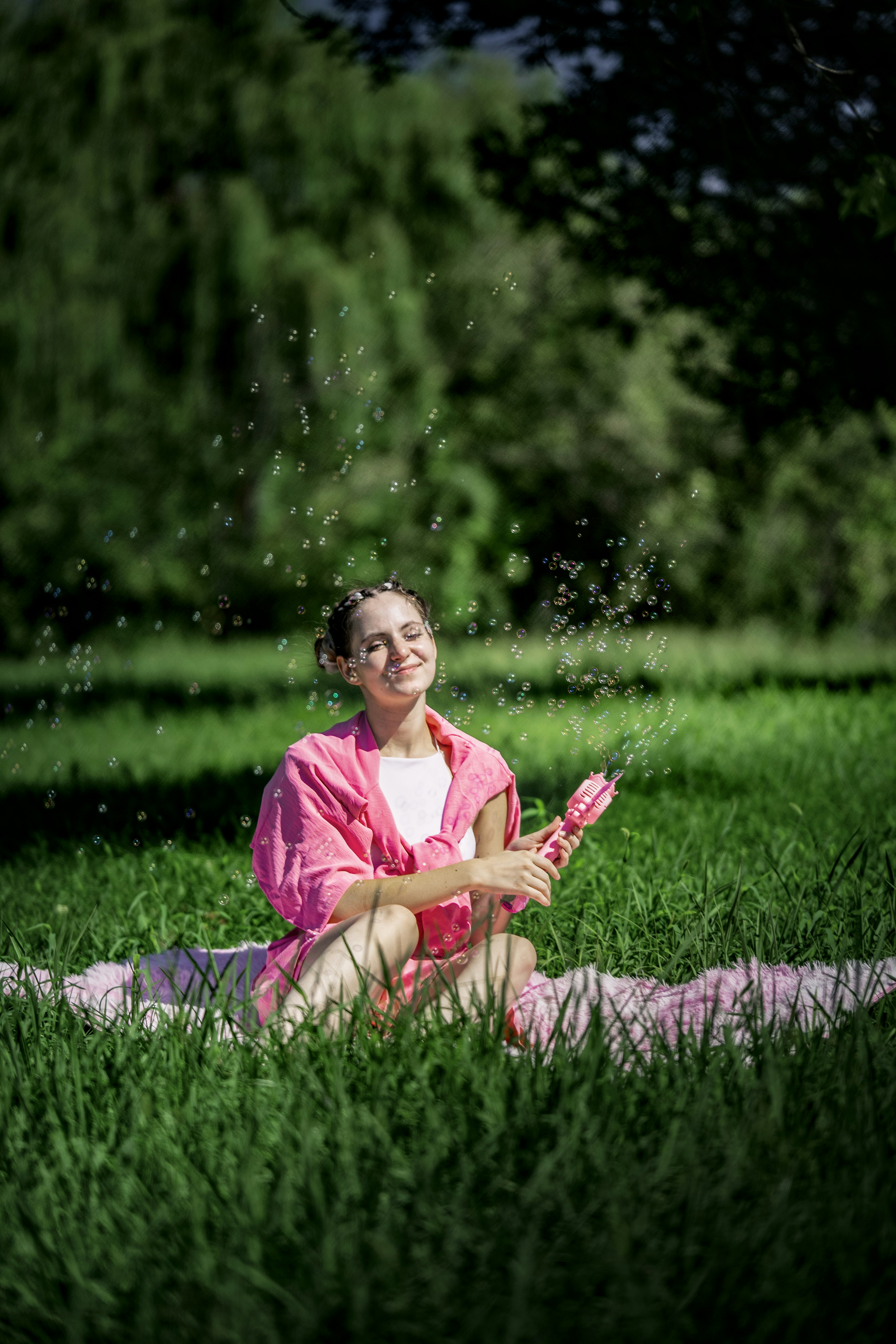 Une femme en chemise rose qui souffle des bulles dans un parc vert