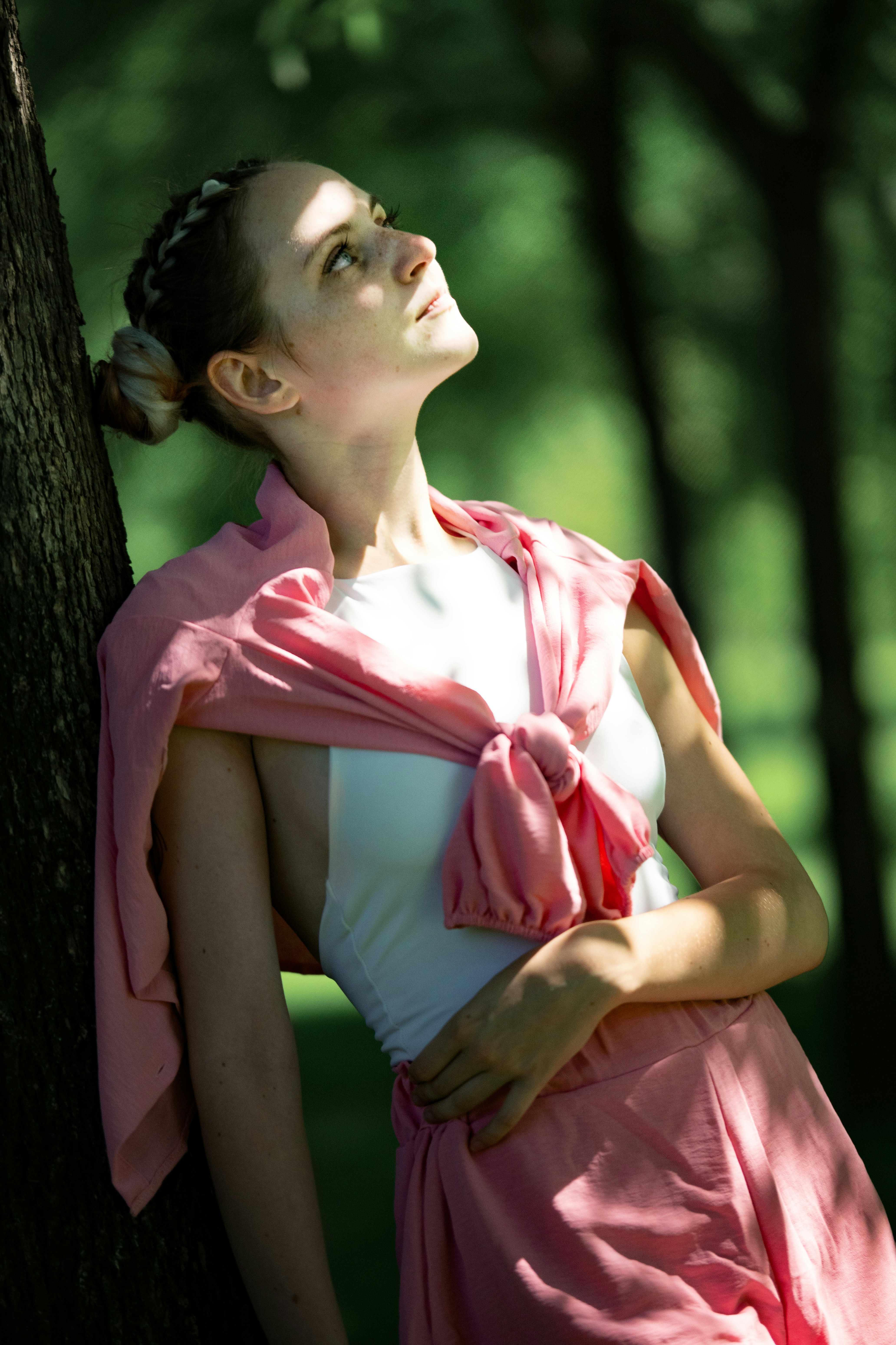 Une femme en haut blanc et pull rose adossée à un arbre