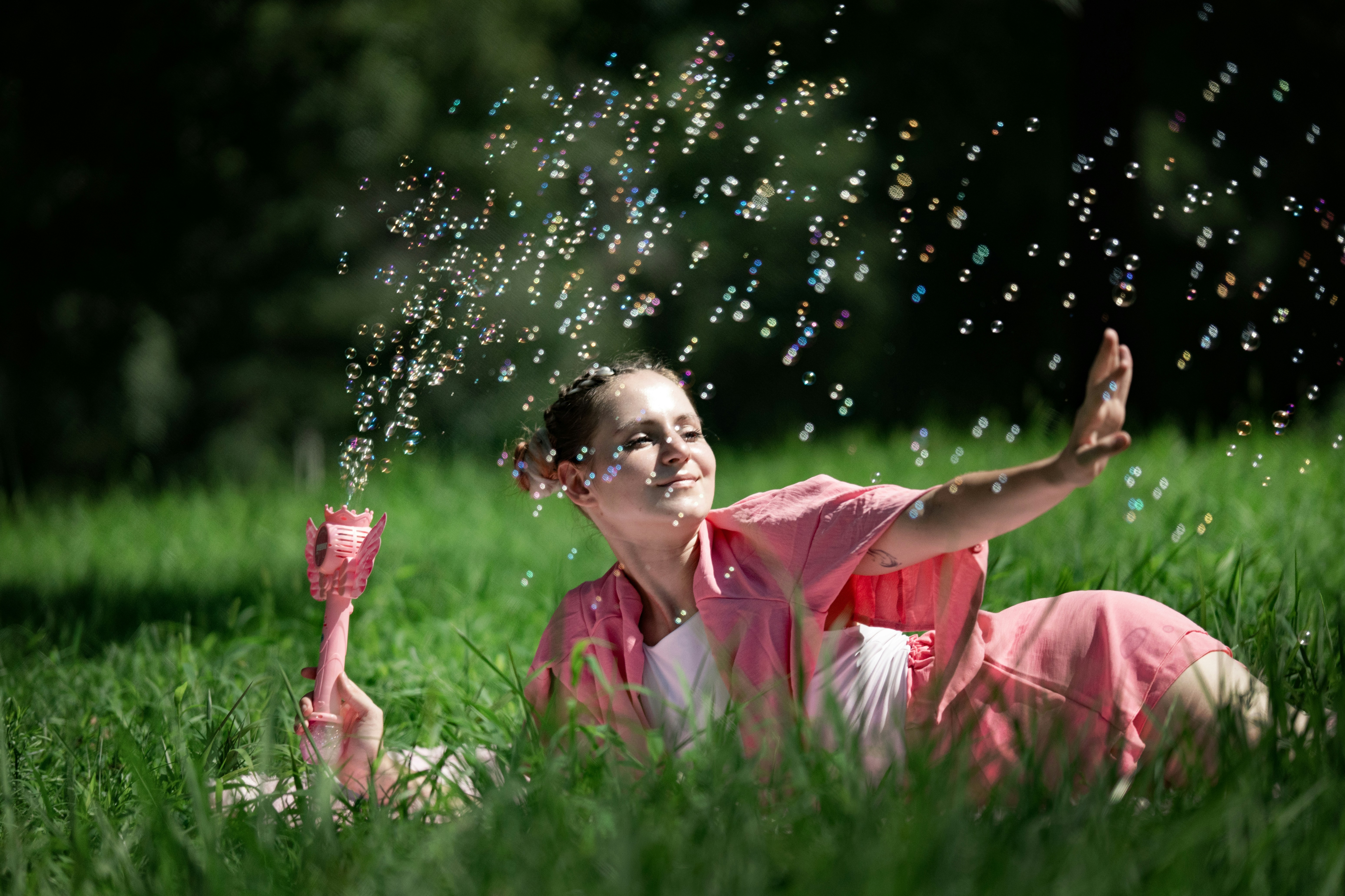 Une femme en tenue rose soufflant des bulles dans un champ vert baigné de soleil
