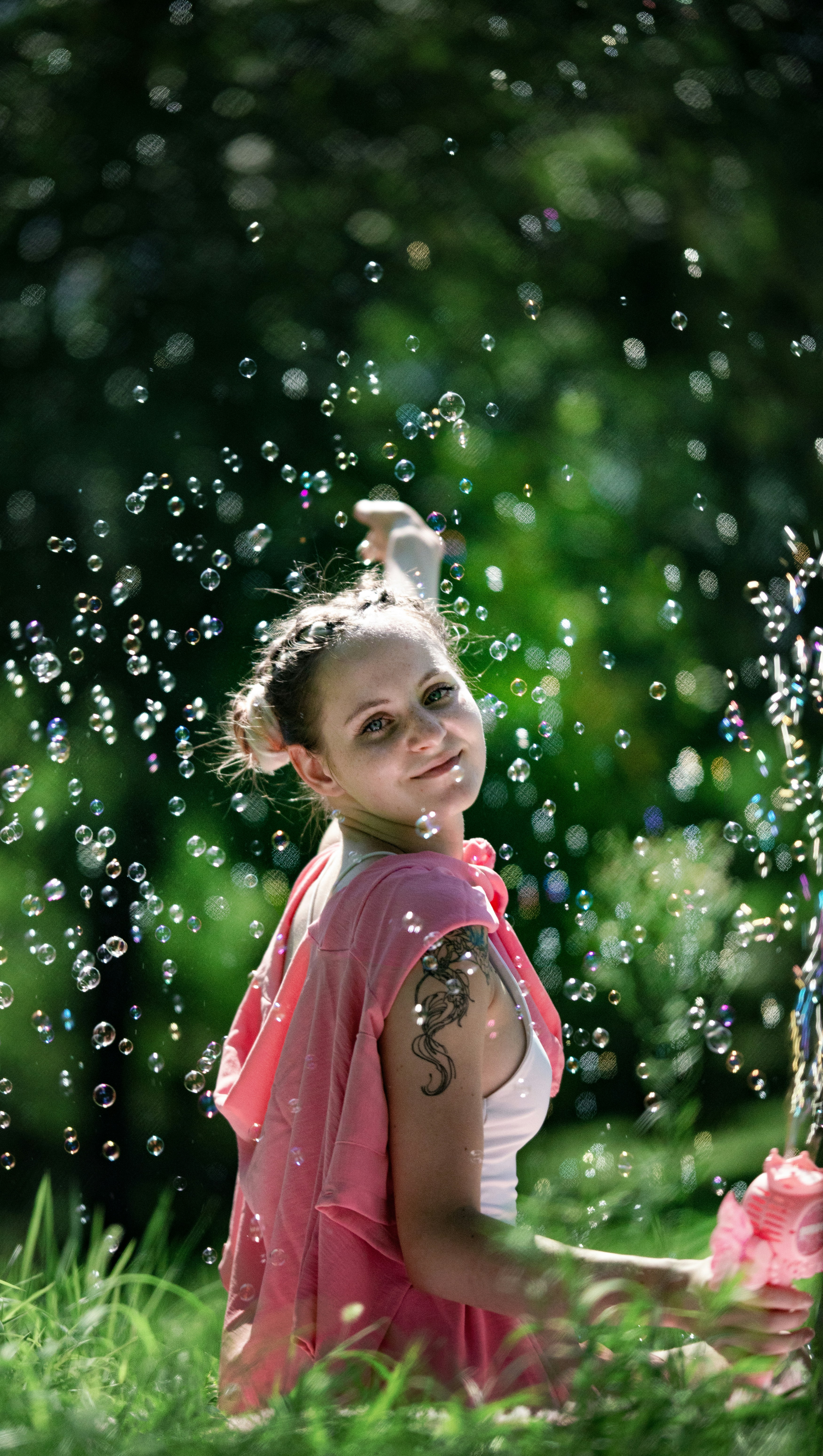 Une femme en sweat à capuche rose entourée de bulles flottantes dans un parc