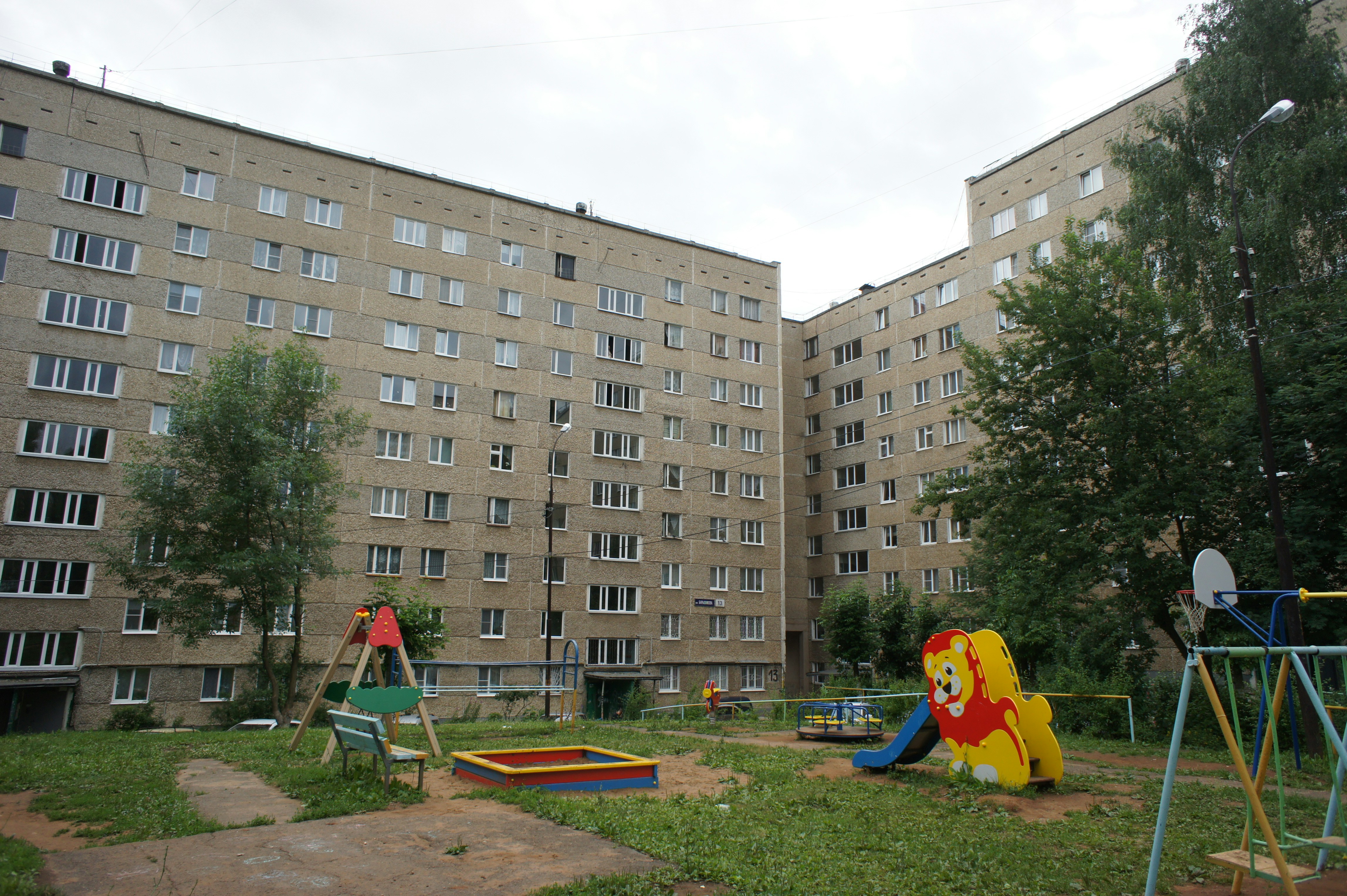 Plac zabaw na podwórku osiedla spółdzielni mieszkaniowej, w tle bloki mieszkalne