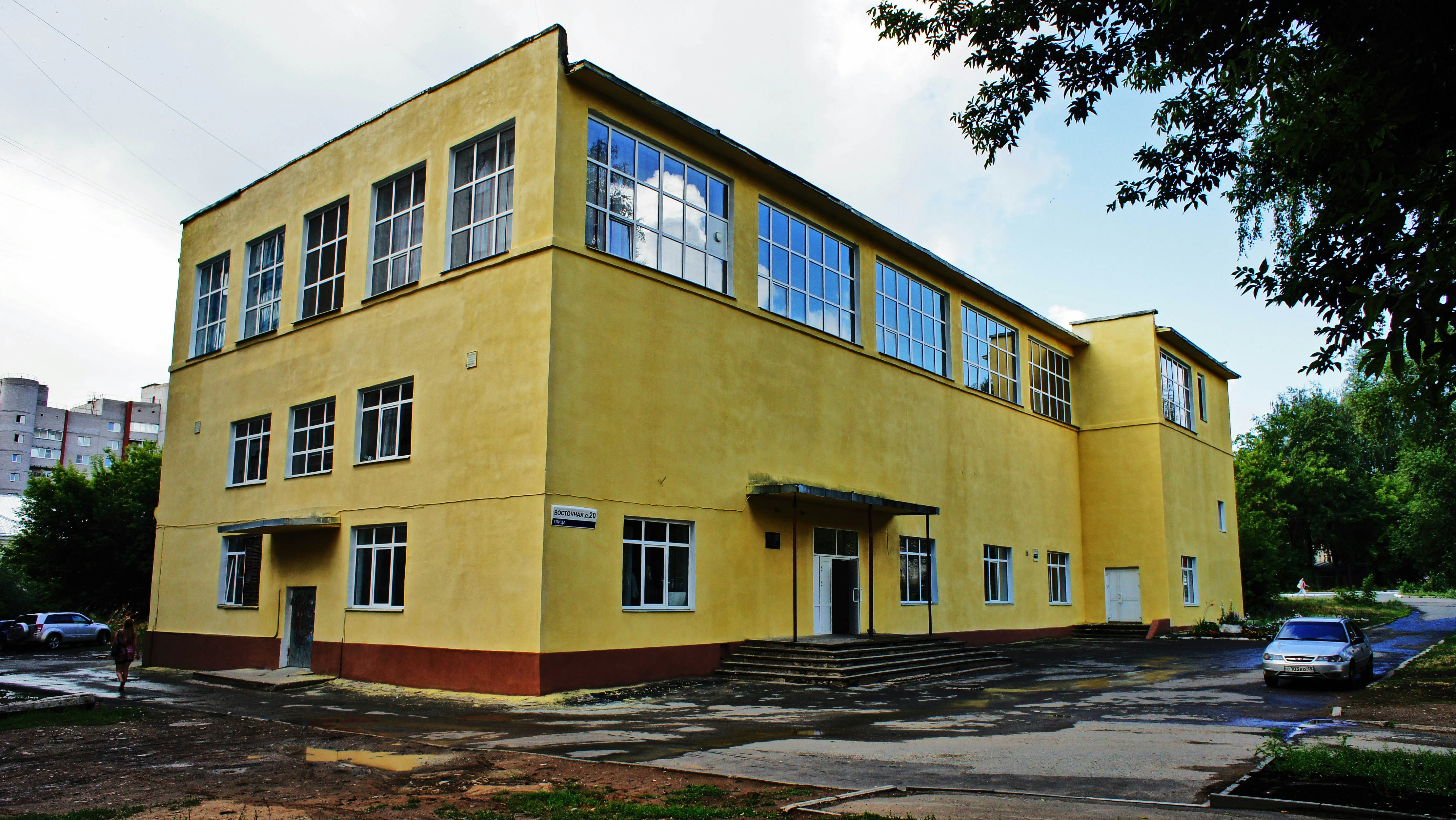 A yellow building with large windows and a brown base on a paved lot