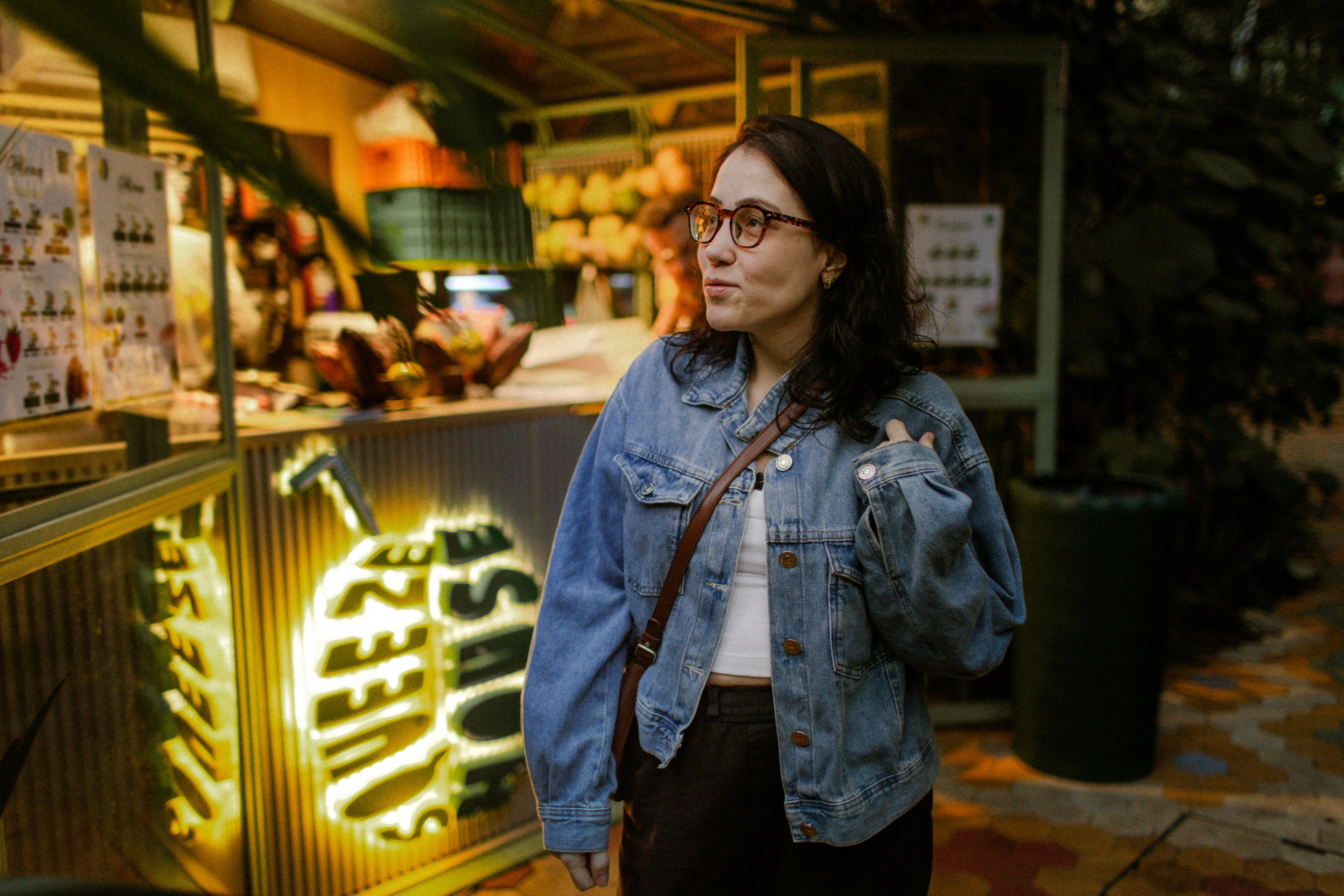 A woman in a denim jacket standing before a glowing juice bar stall
