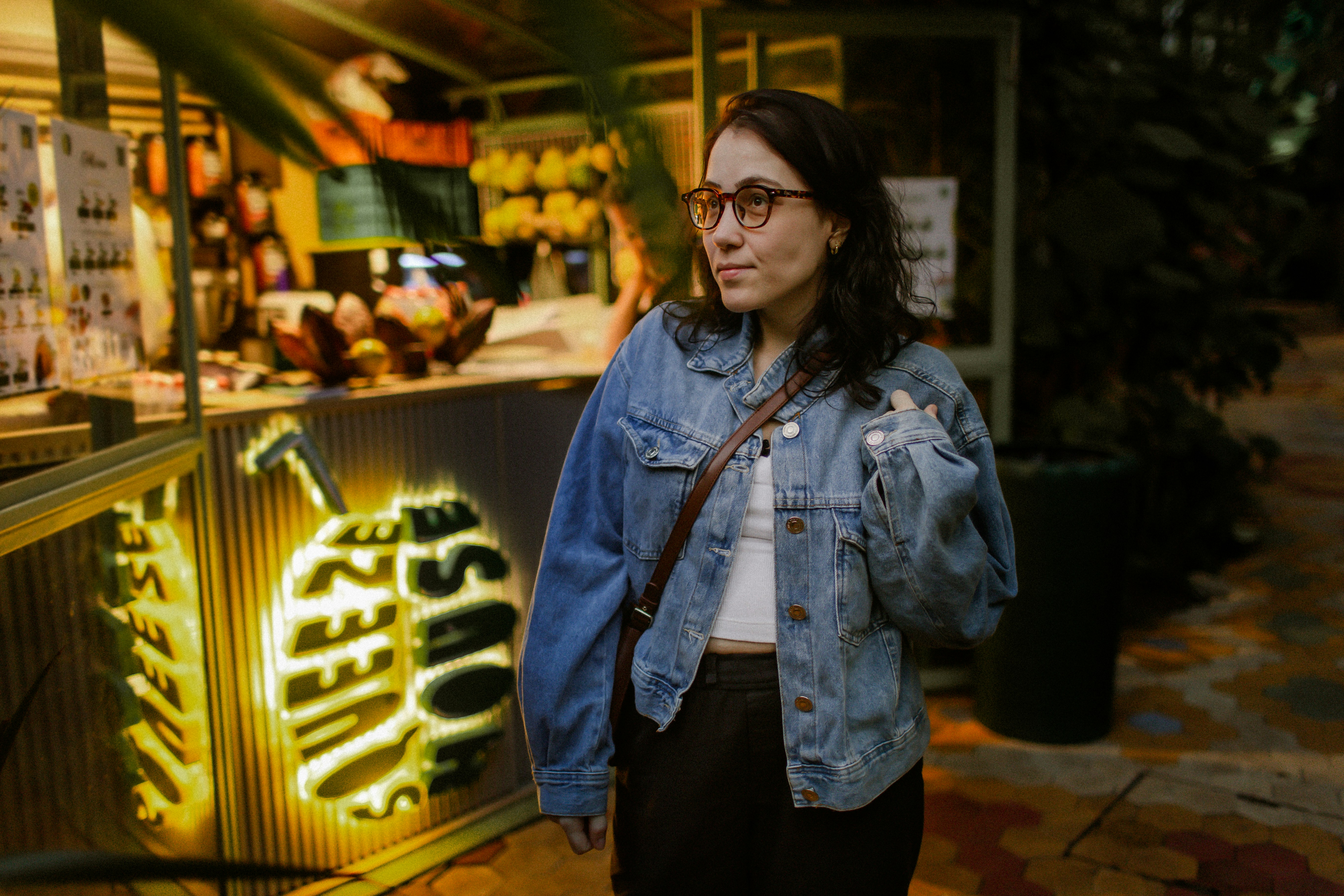 A woman in a denim jacket standing beside a glowing yellow juice stand