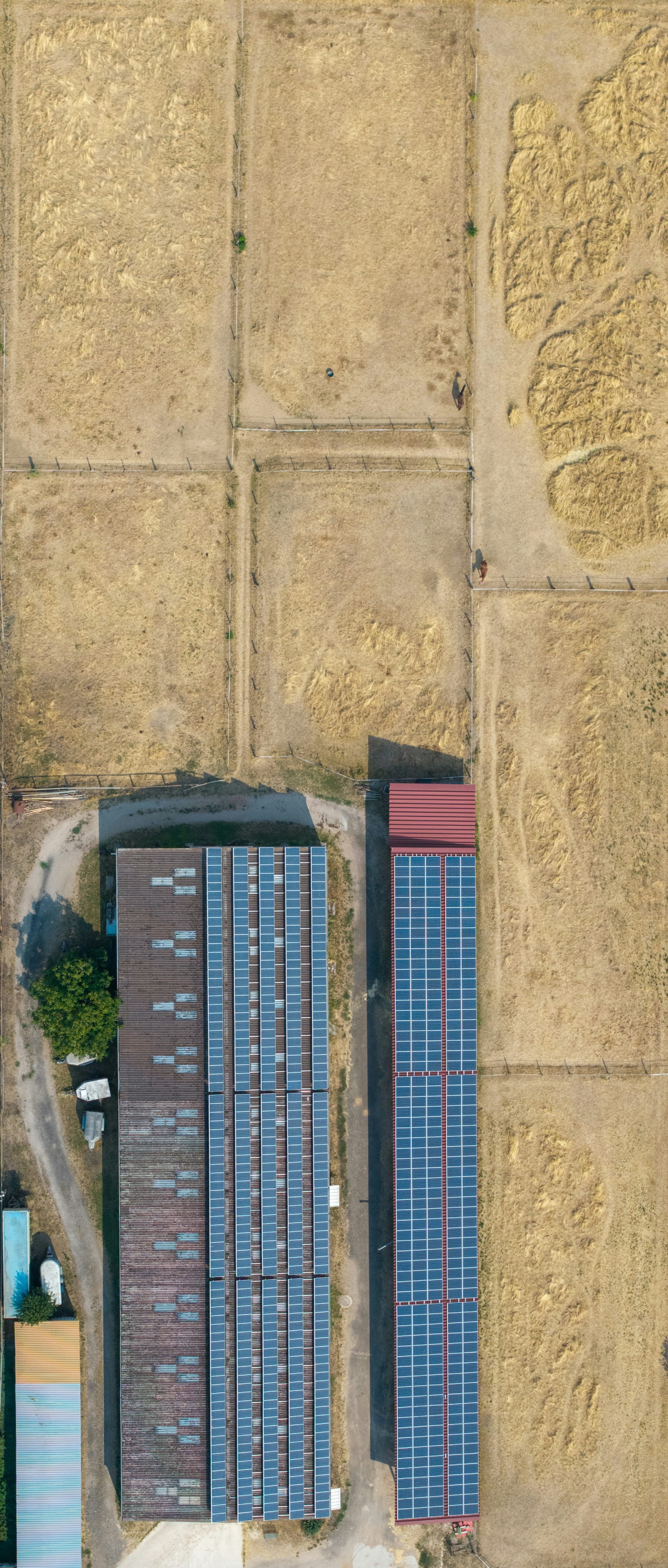 Aerial view of two buildings with solar panels in a dry grassy field