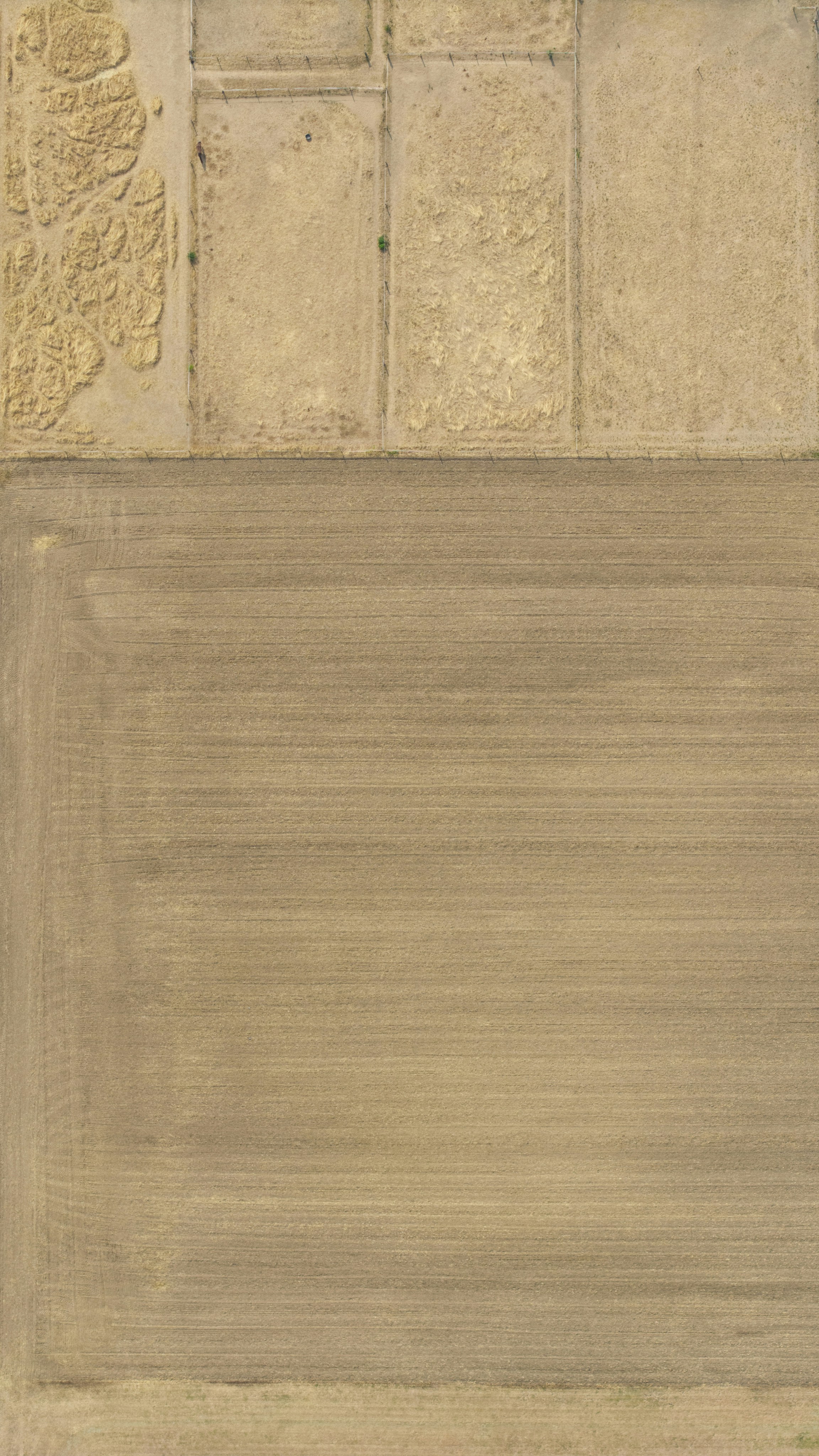 An aerial view of a large tilled field beside several dry fenced paddocks