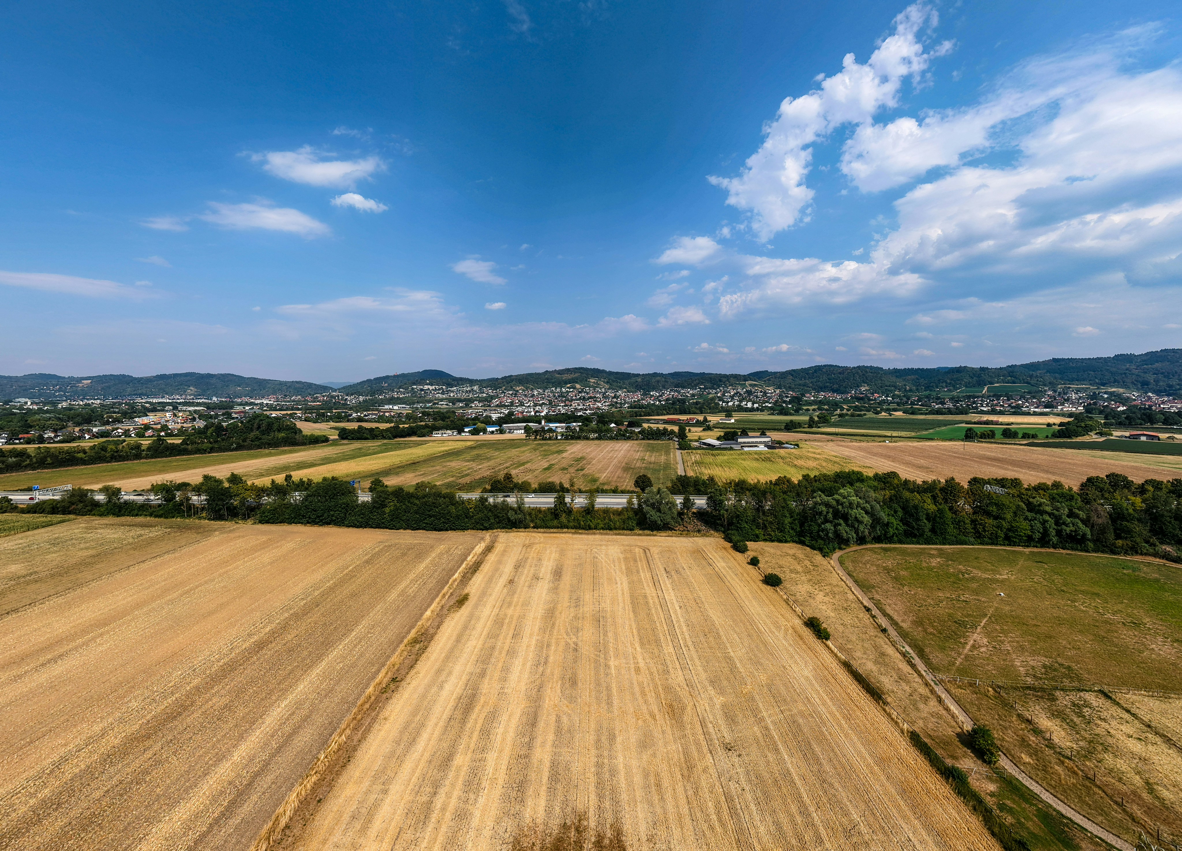 An aerial view of golden harvested fields and a distant town under a blue sky