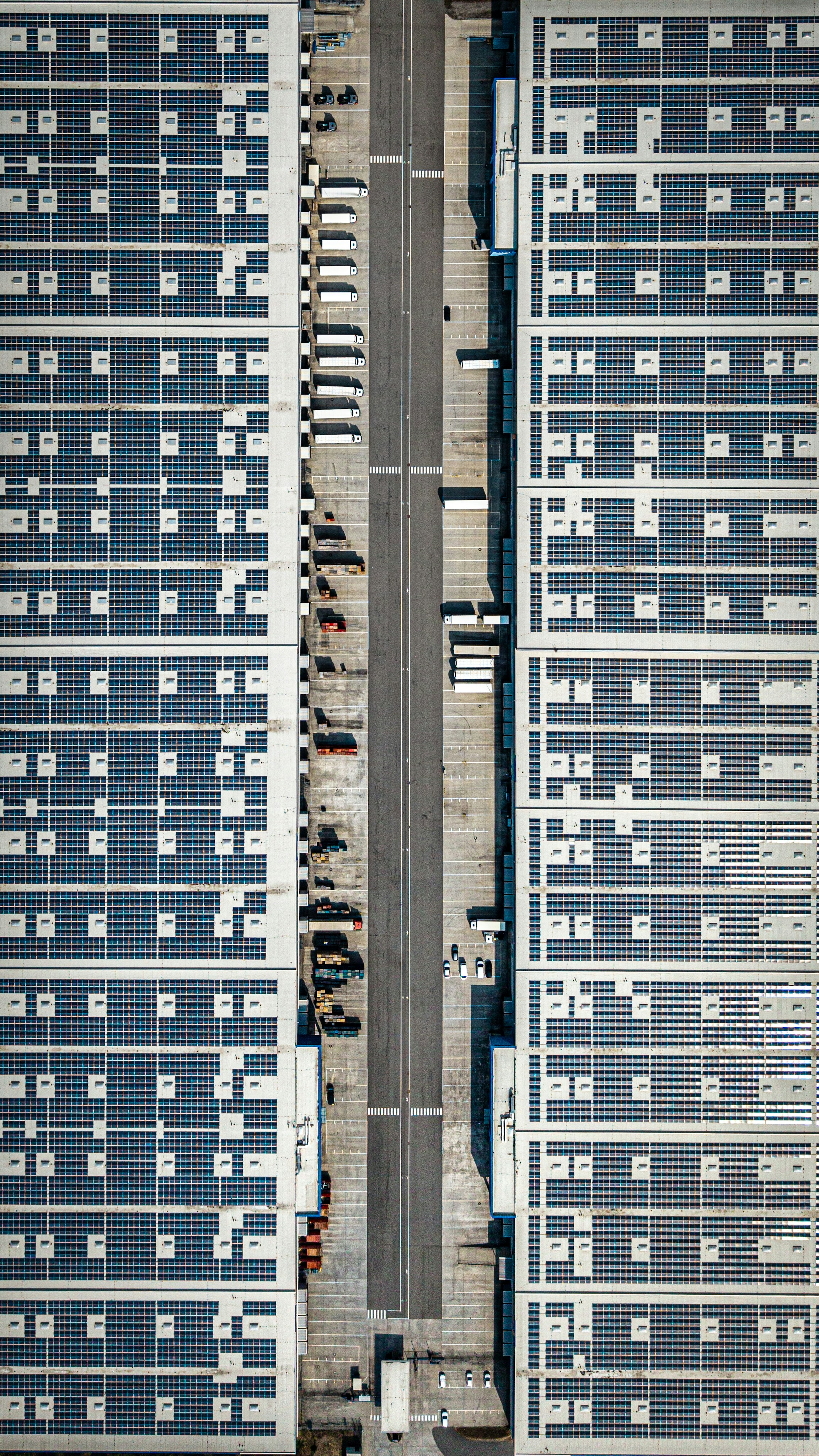 Aerial view of two large warehouse roofs covered in solar panels with trucks parked below