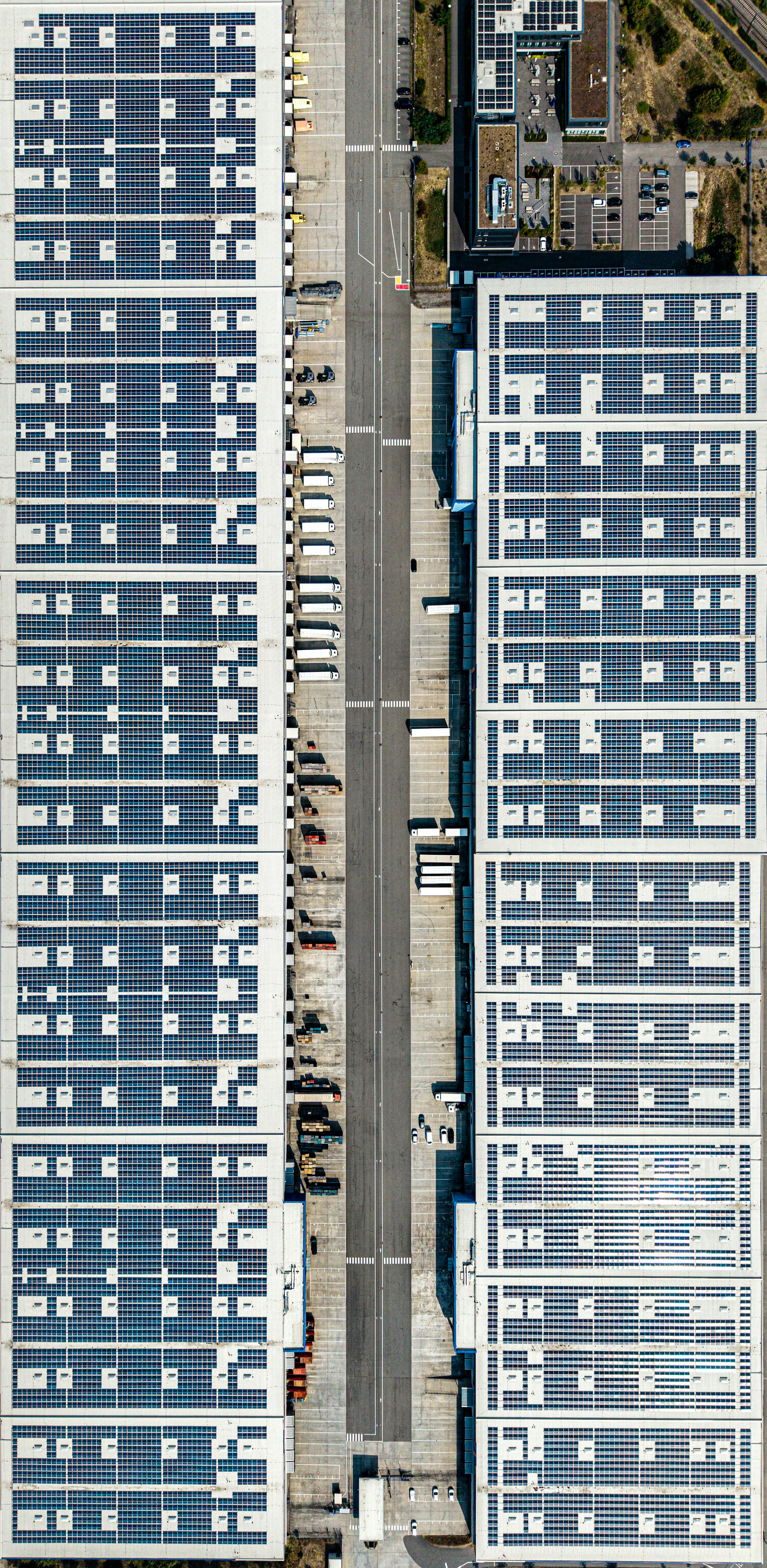 Aerial view of two large warehouse roofs covered in solar panels with trucks parked