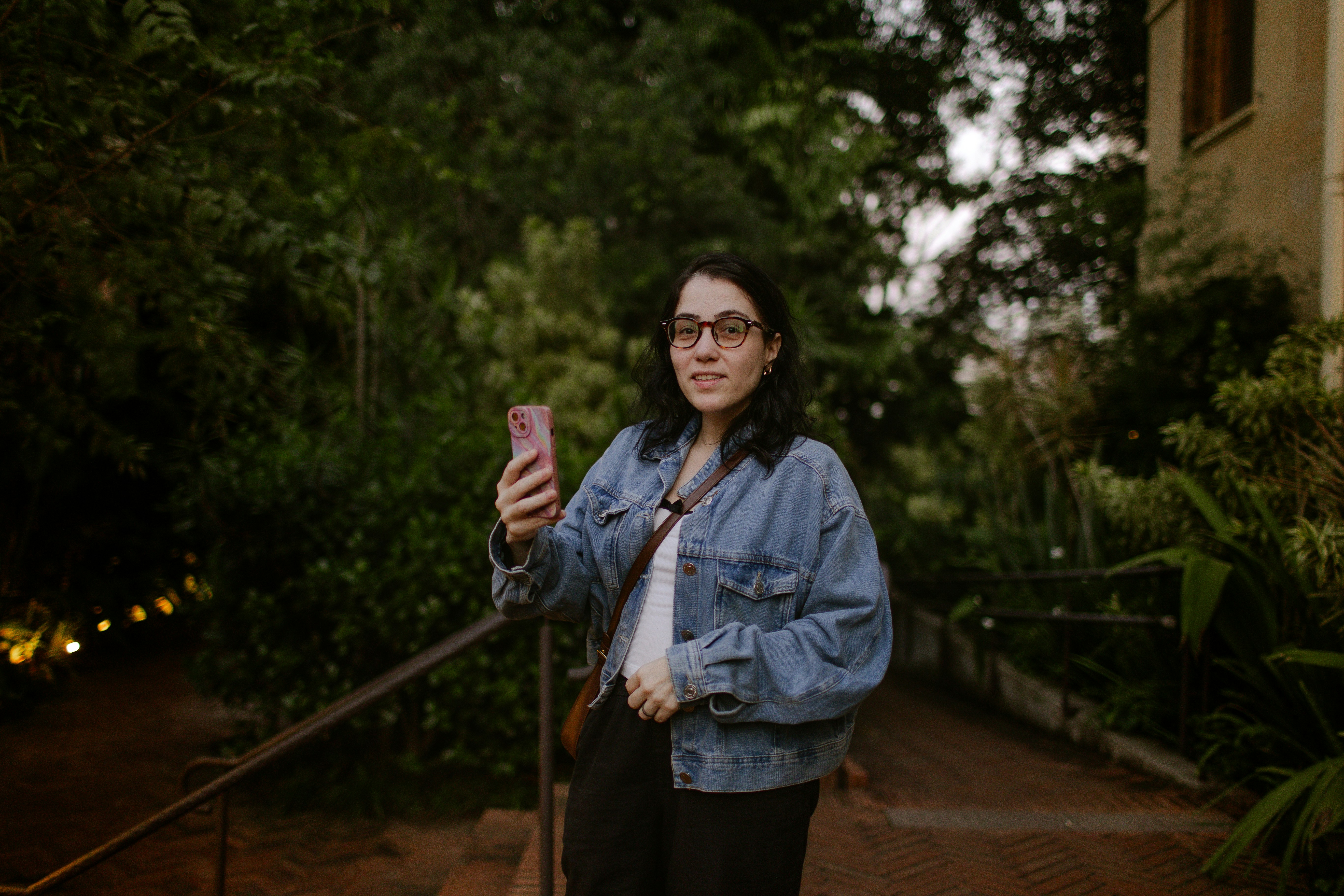 A woman in a denim jacket holding a smartphone in a lush garden