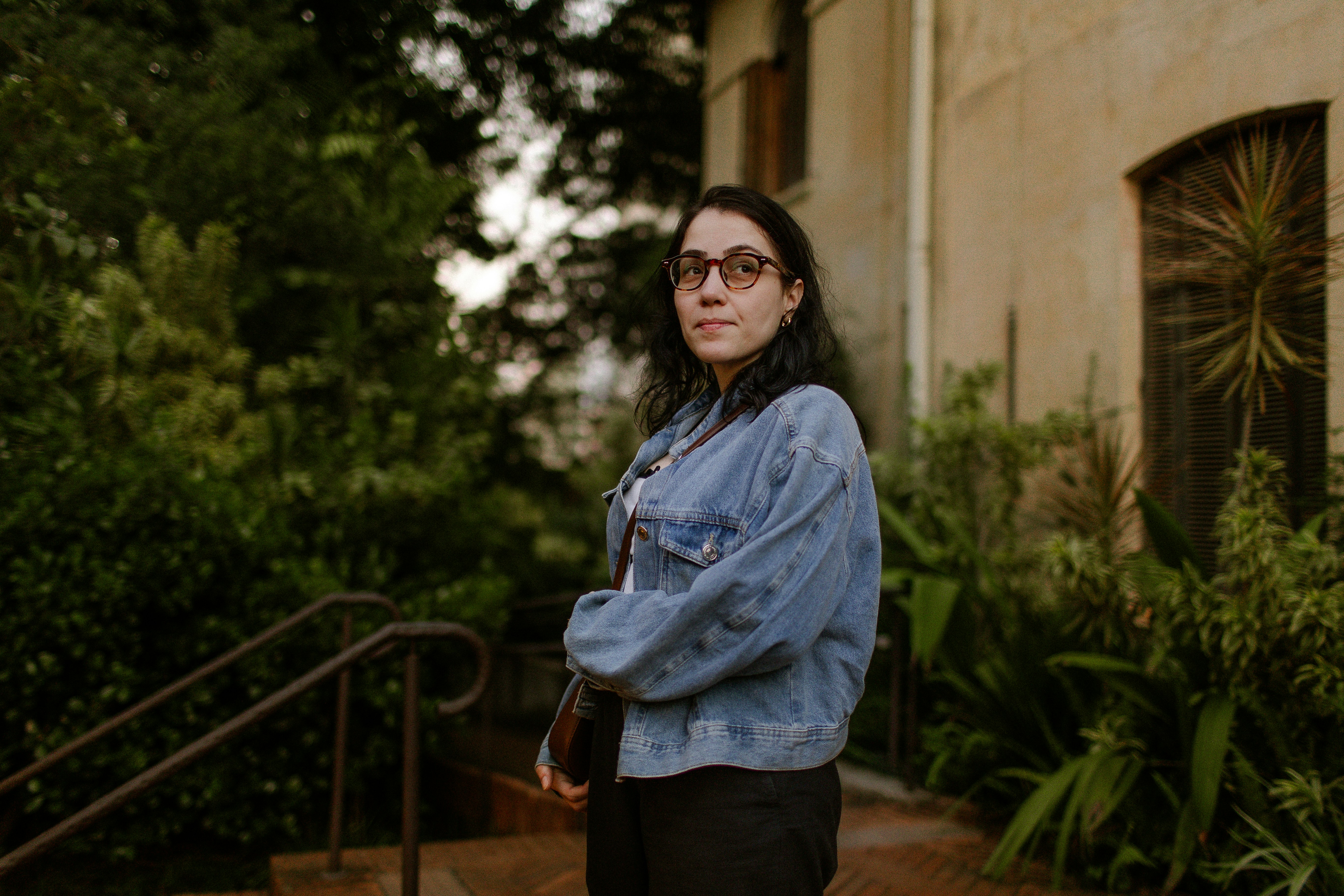 A woman in a denim jacket and glasses outdoors near a building