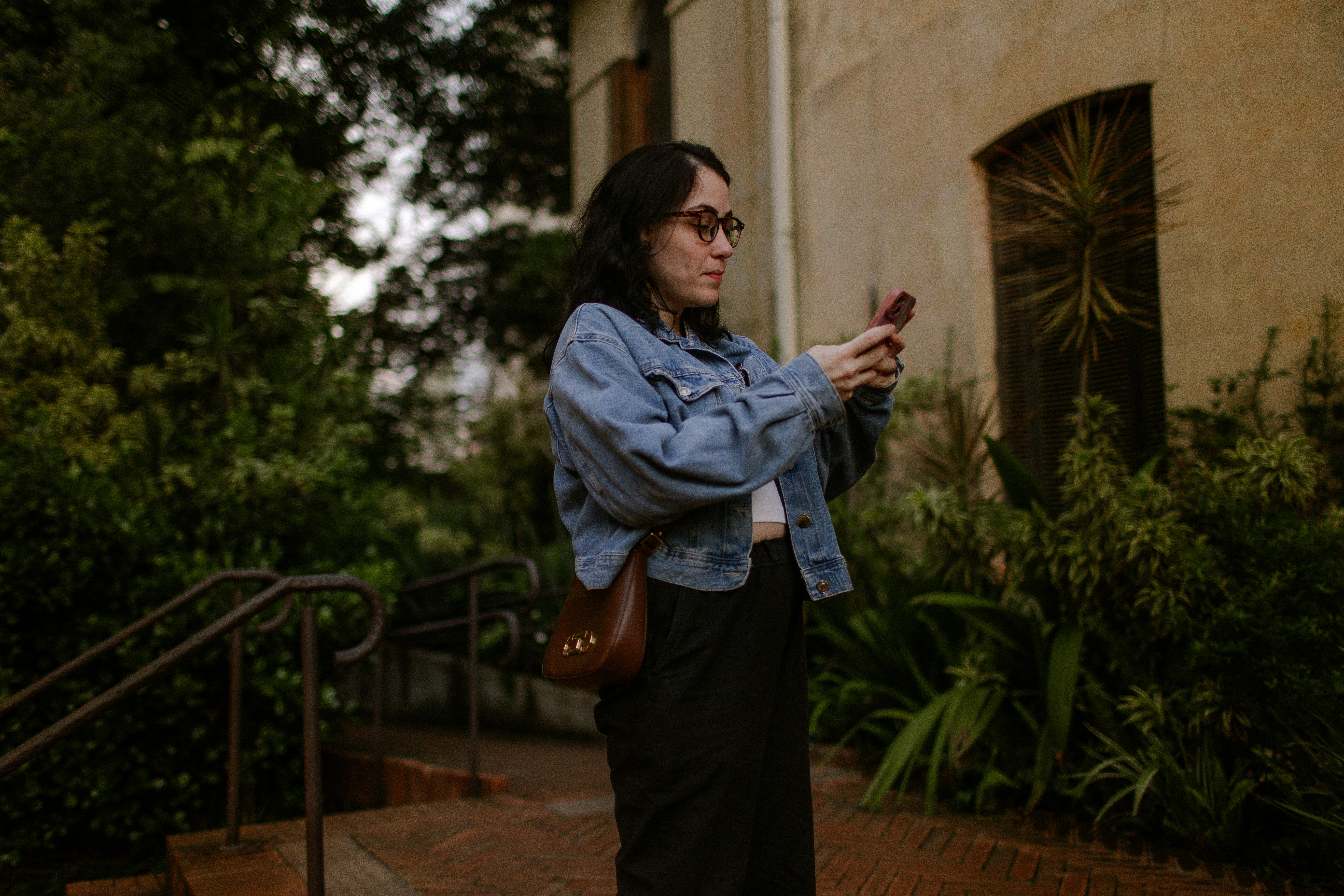 A woman in a denim jacket using a smartphone in a garden