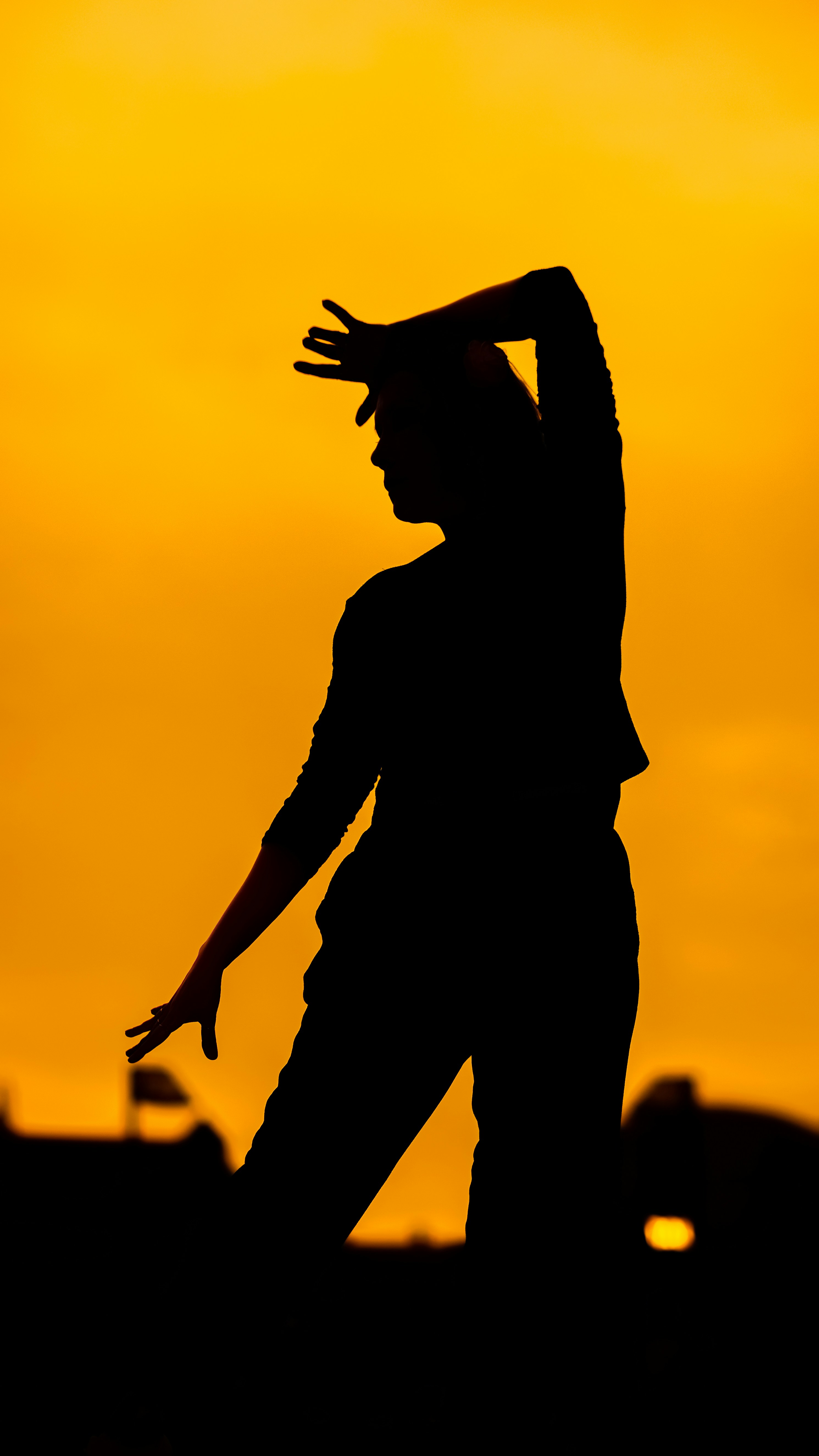 A person in silhouette against a vibrant orange sky with arms raised