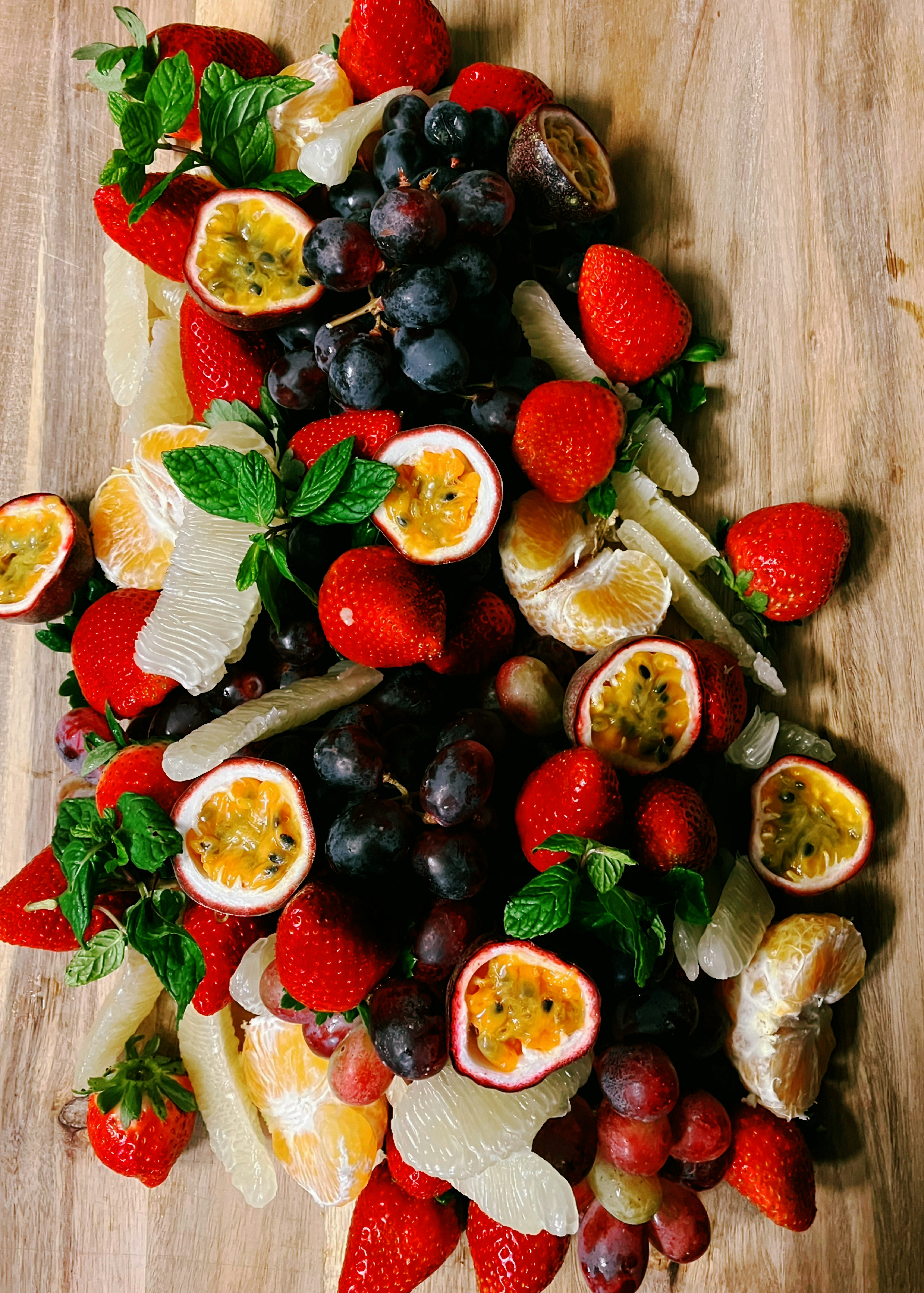 Strawberries, passion fruit, grapes, and citrus segments with mint on a wooden board