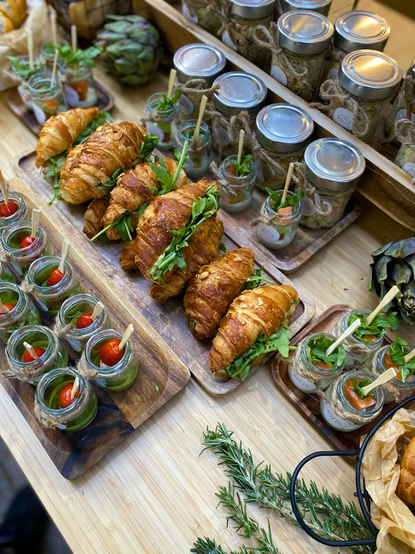 Catering spread of croissant sandwiches and small jars on wooden boards