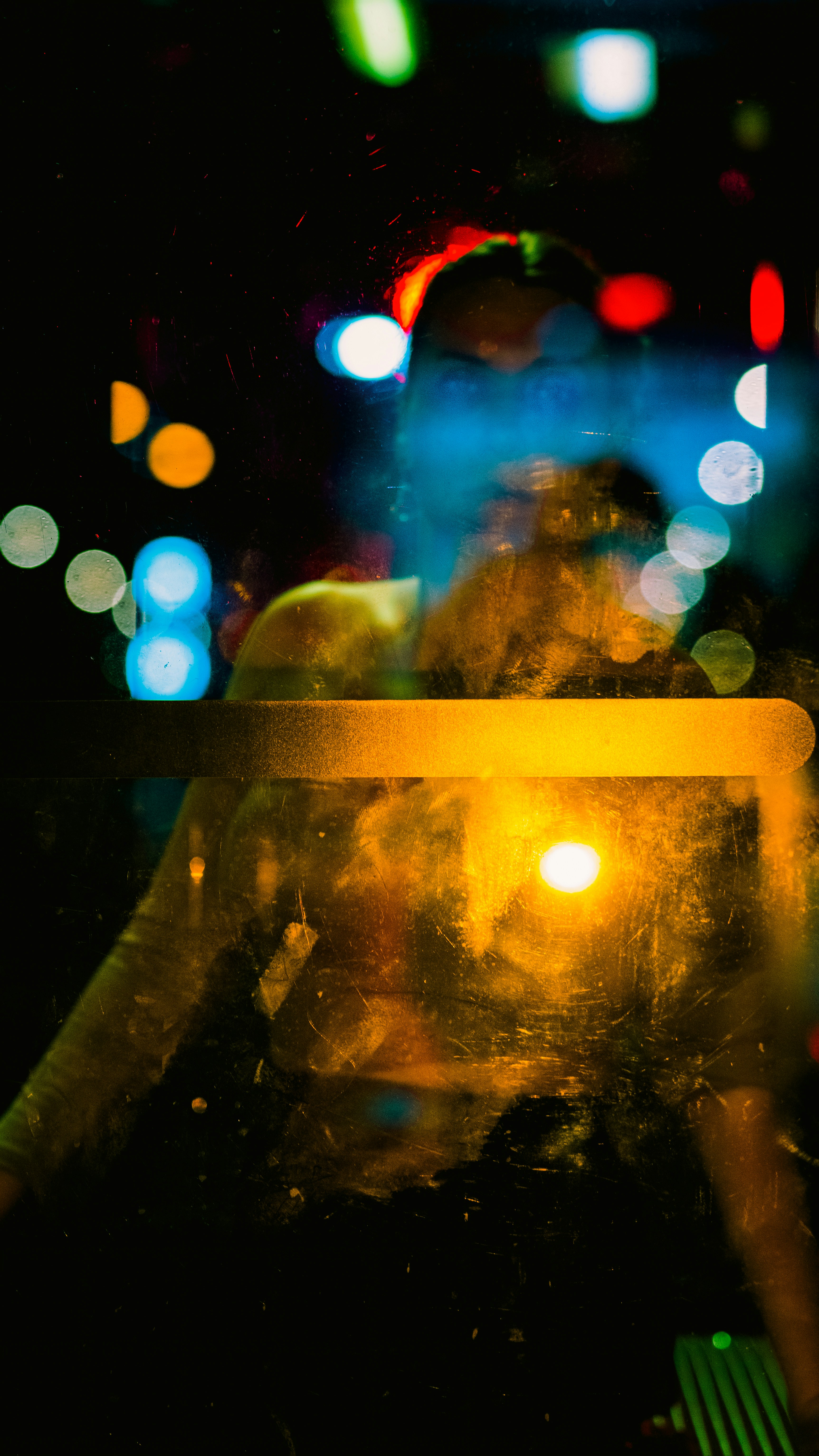A person reflected in a scratched glass door with colorful bokeh city lights