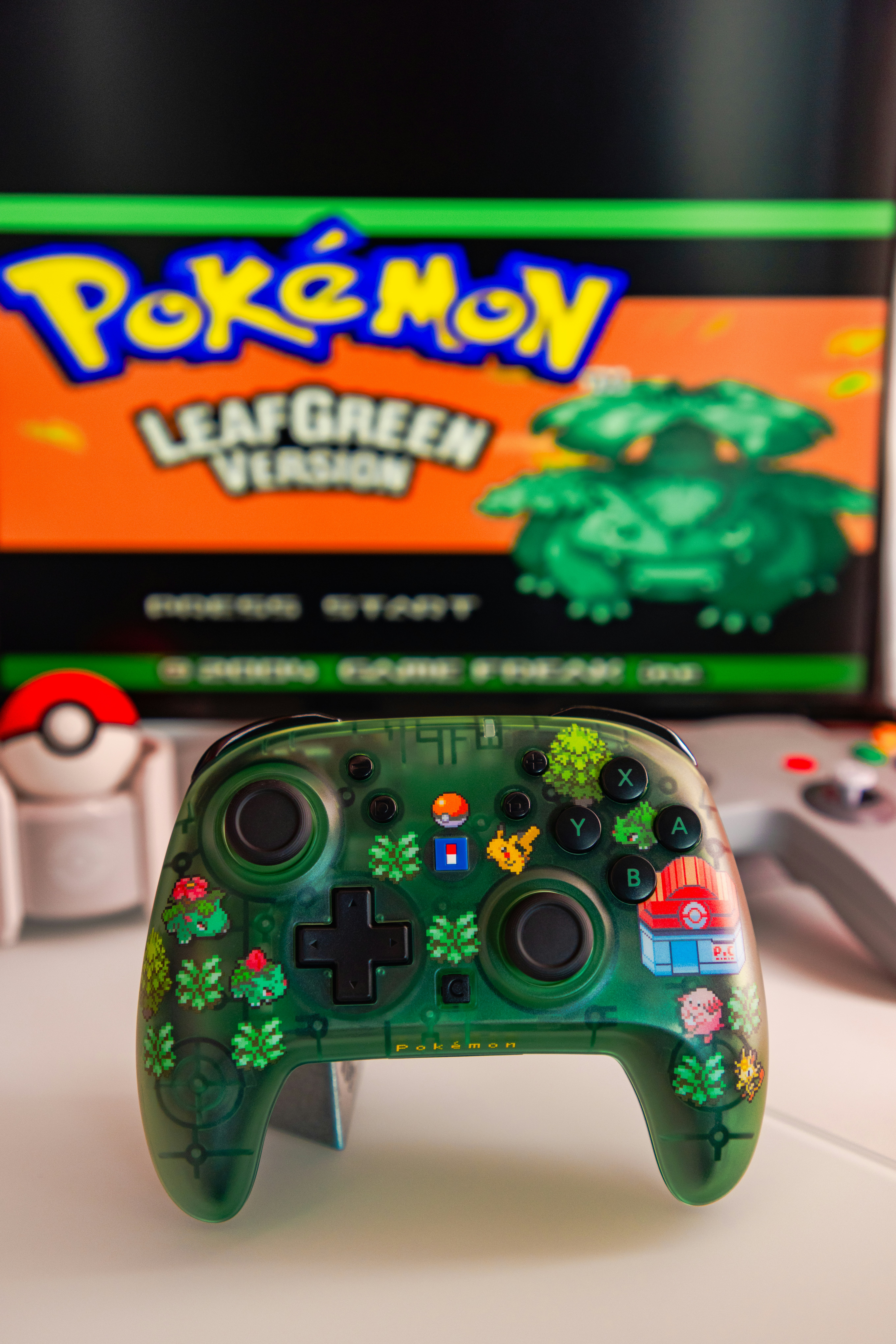 A green translucent video game controller in front of a screen displaying Pokemon LeafGreen