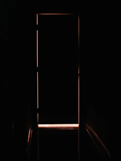A closed door outlined by a thin sliver of warm orange light