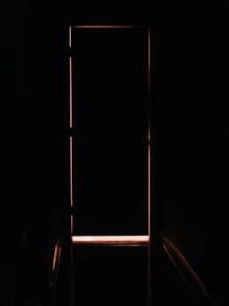 A closed door outlined by a thin sliver of warm orange light