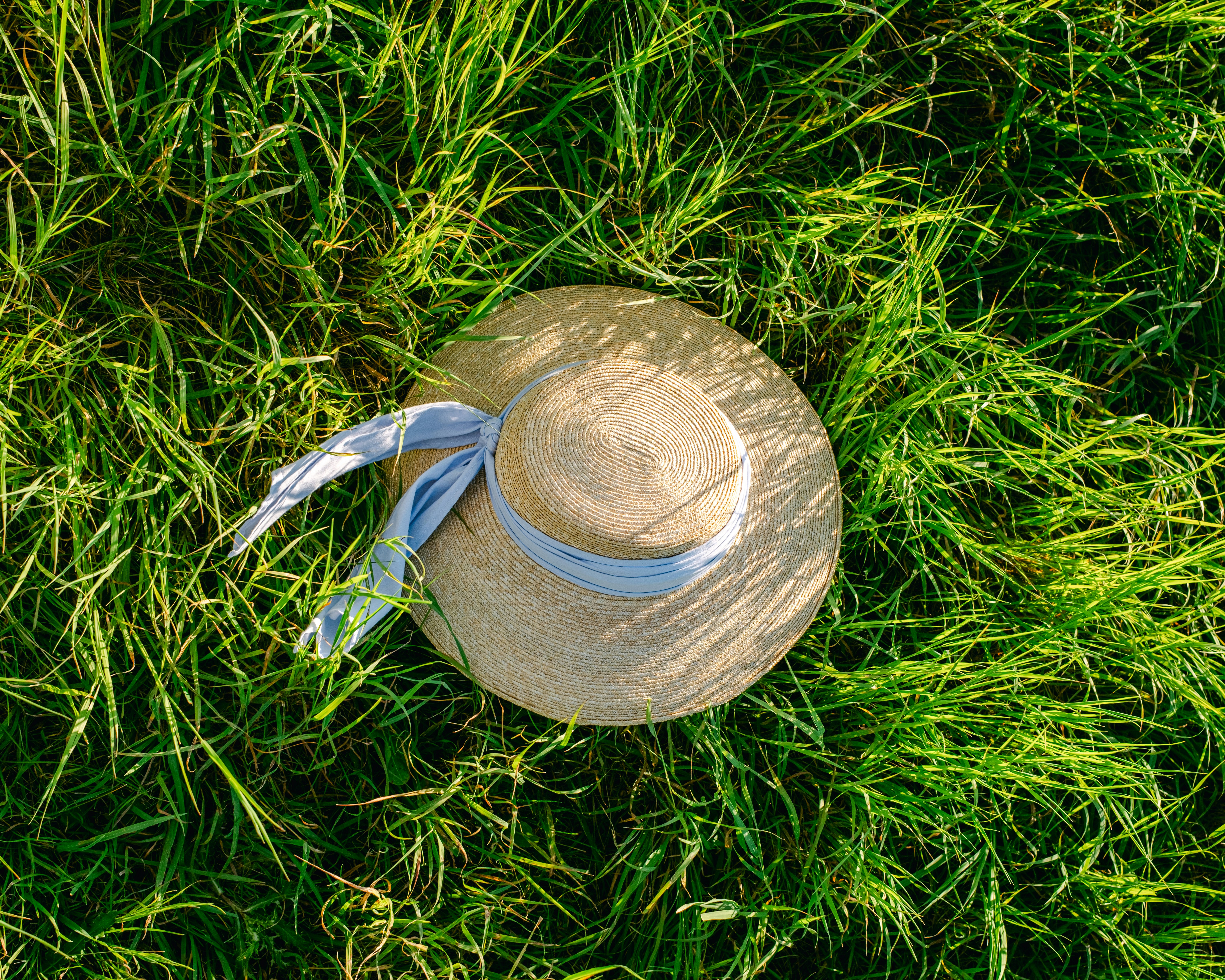 Un sombrero de paja con una cinta azul claro descansando sobre hierba verde vibrante