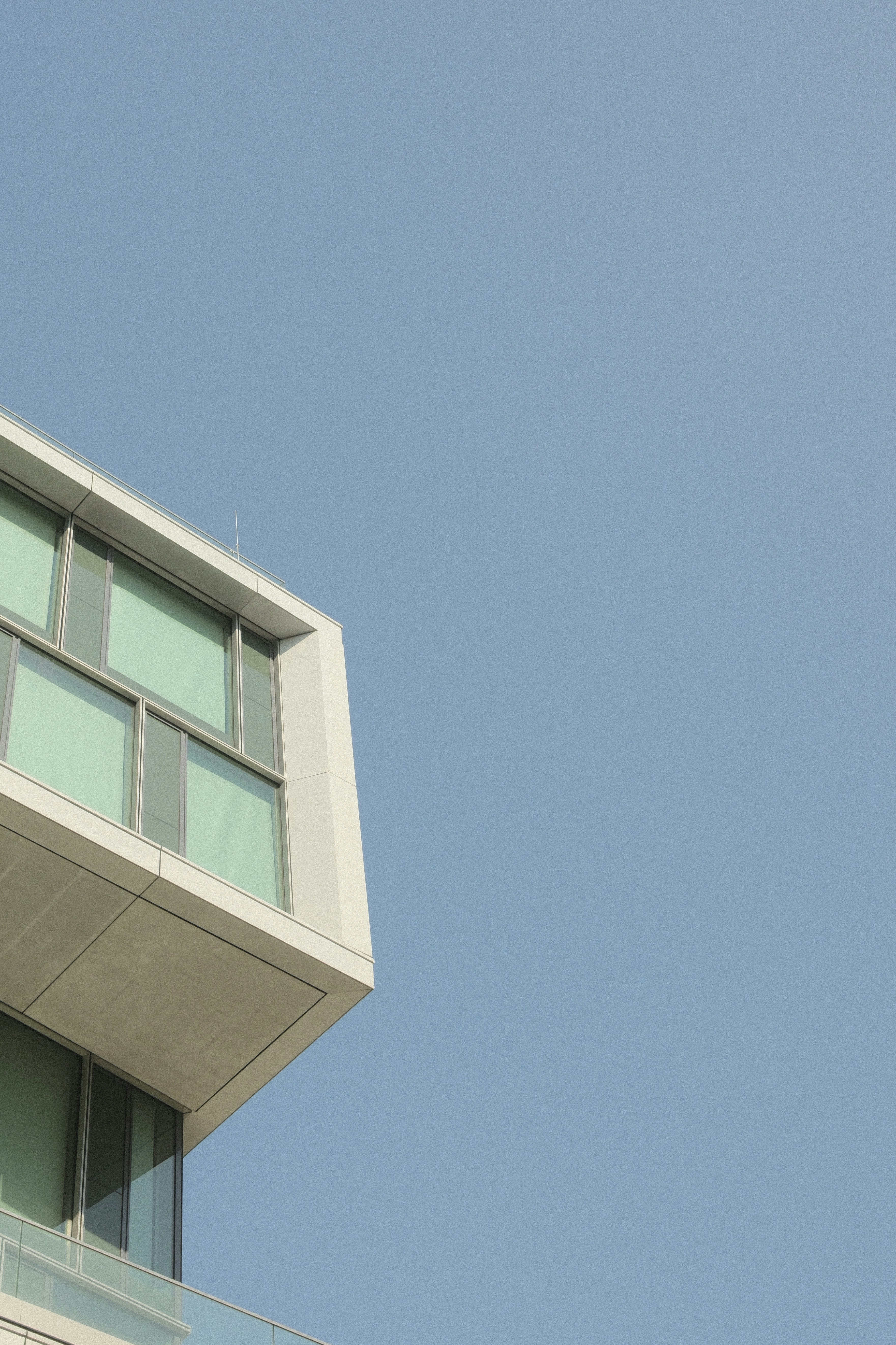 A corner of a modern white building with glass windows against a clear sky