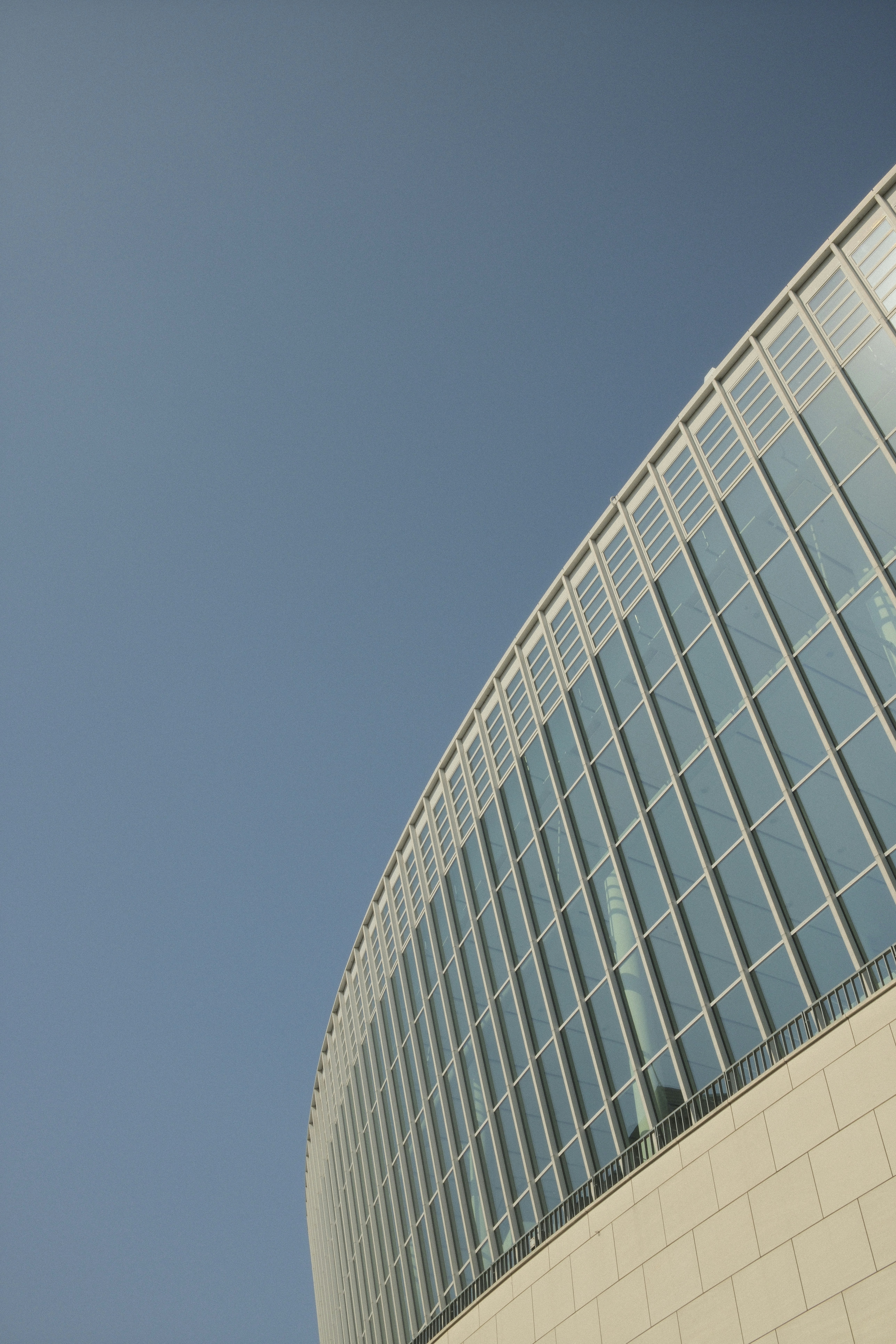 A curved glass facade of a modern building against a clear blue sky - 相关推荐