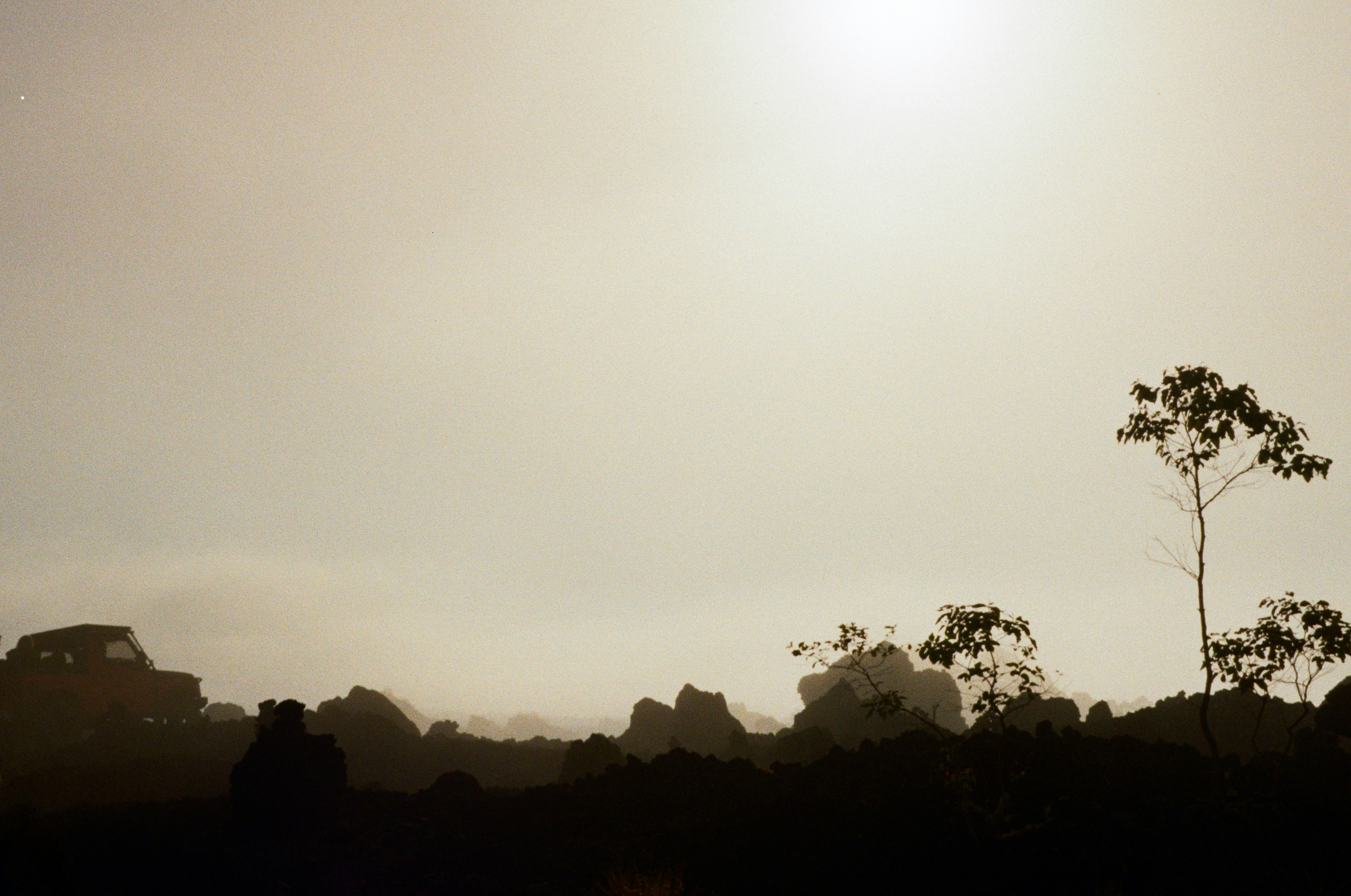 A vehicle silhouette on a rocky horizon against a bright hazy sky
