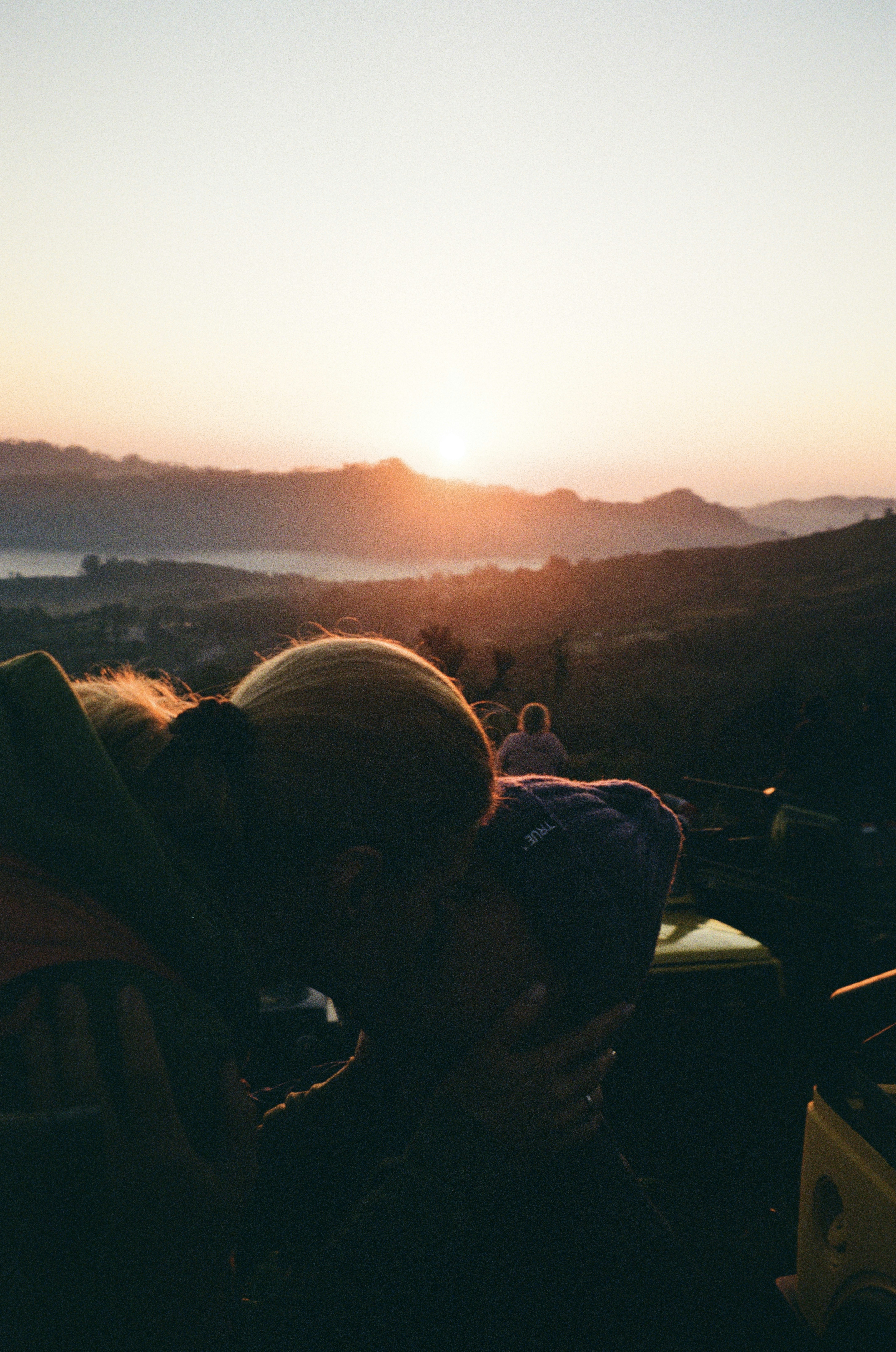 Two people kissing in silhouette against a warm orange sky and distant hills