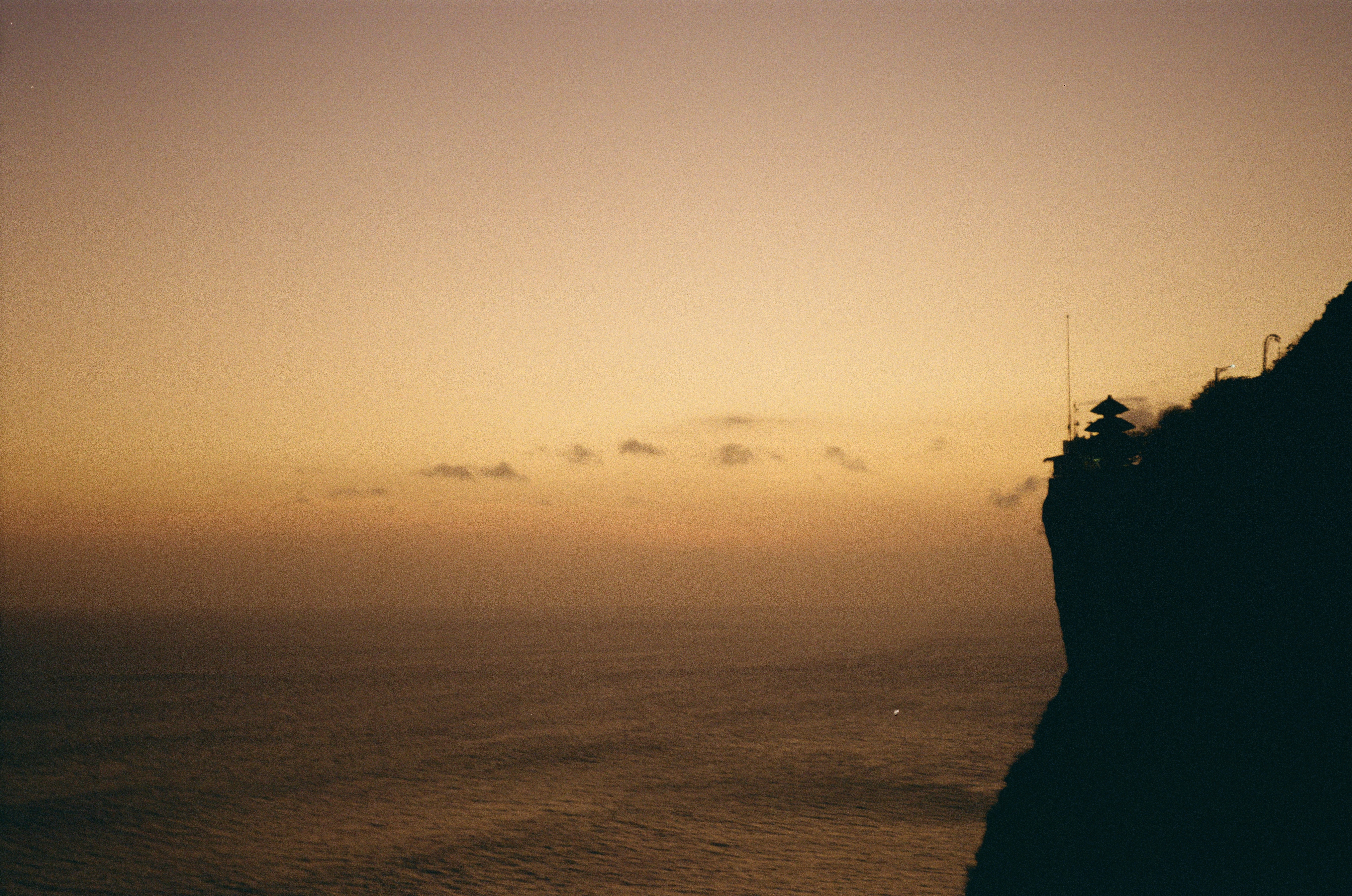 A temple silhouette on a cliff edge above the ocean at golden hour