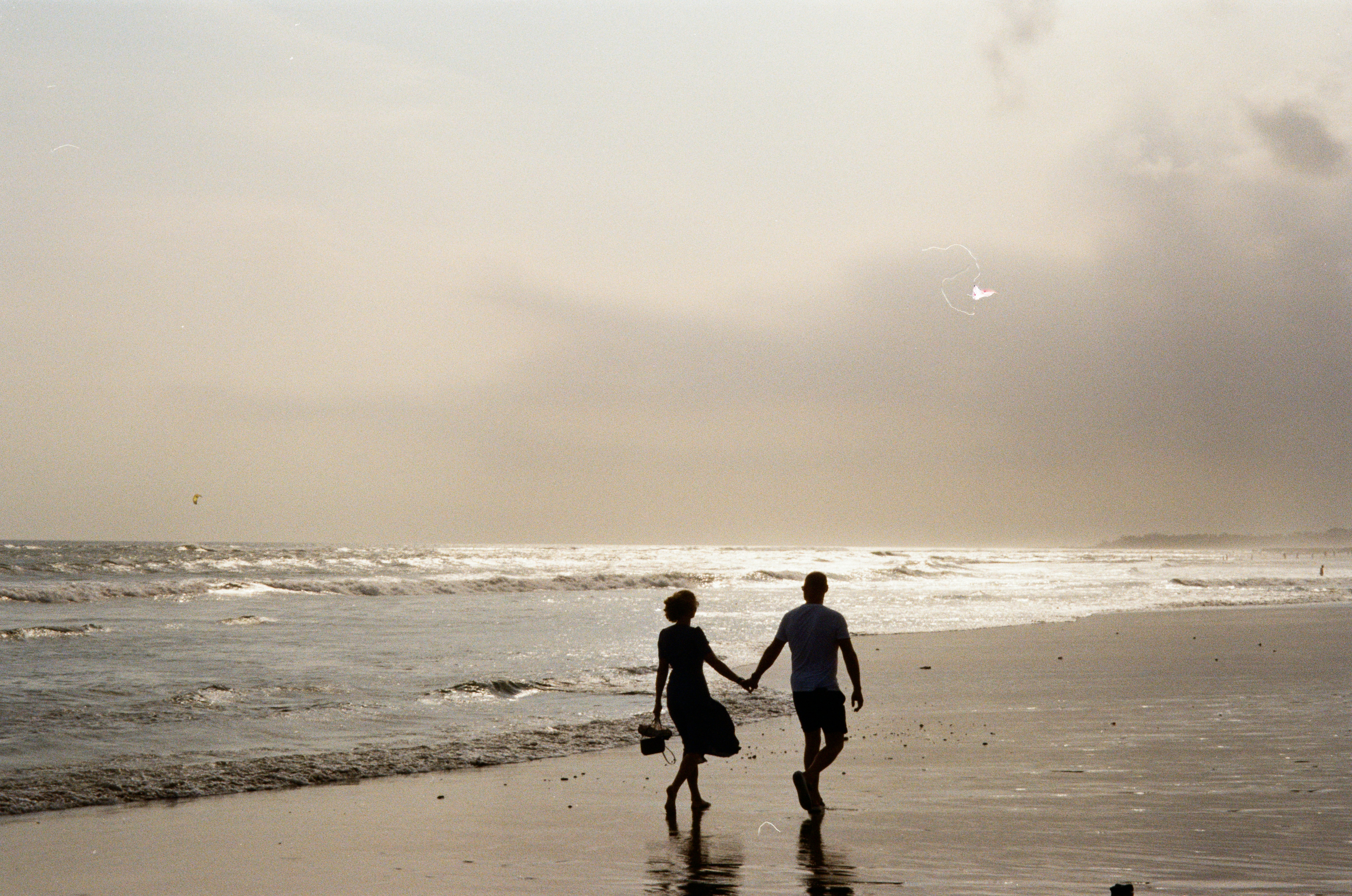 A person in a dress and a person in shorts holding hands on a beach