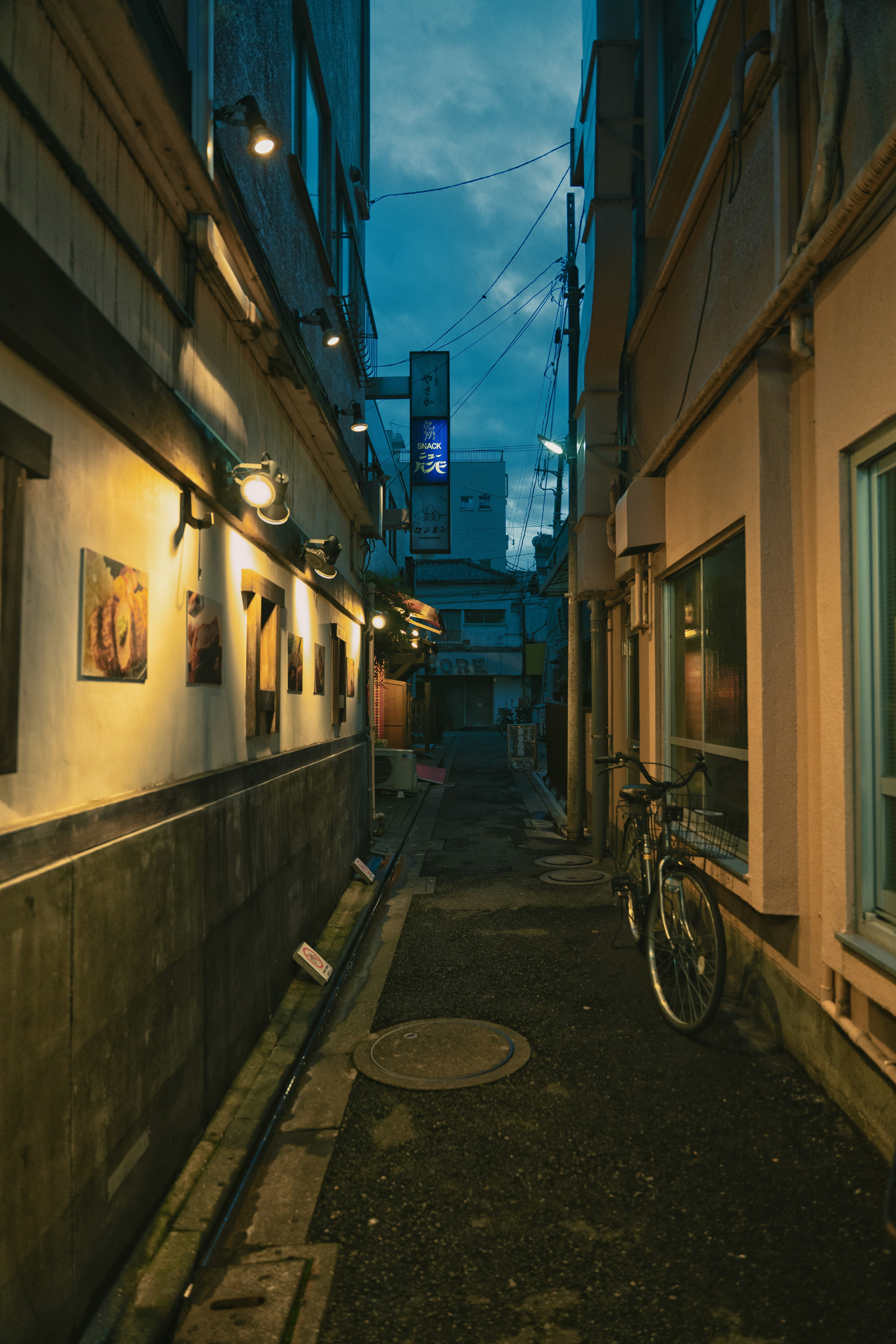 A narrow alleyway in Japan at dusk with a bicycle parked against a wall