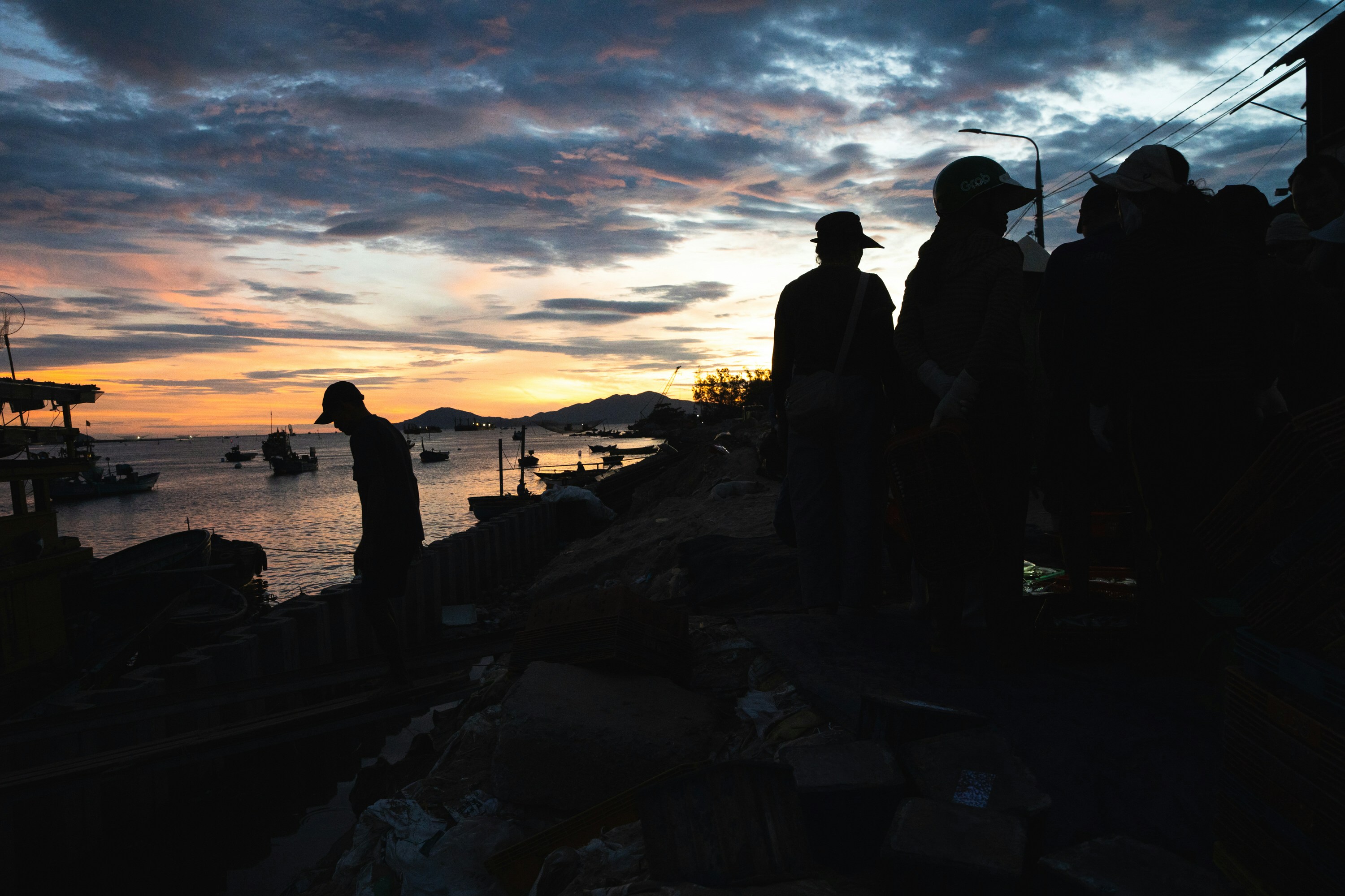 Silhouettes of people on a harbor shore against a warm orange sky