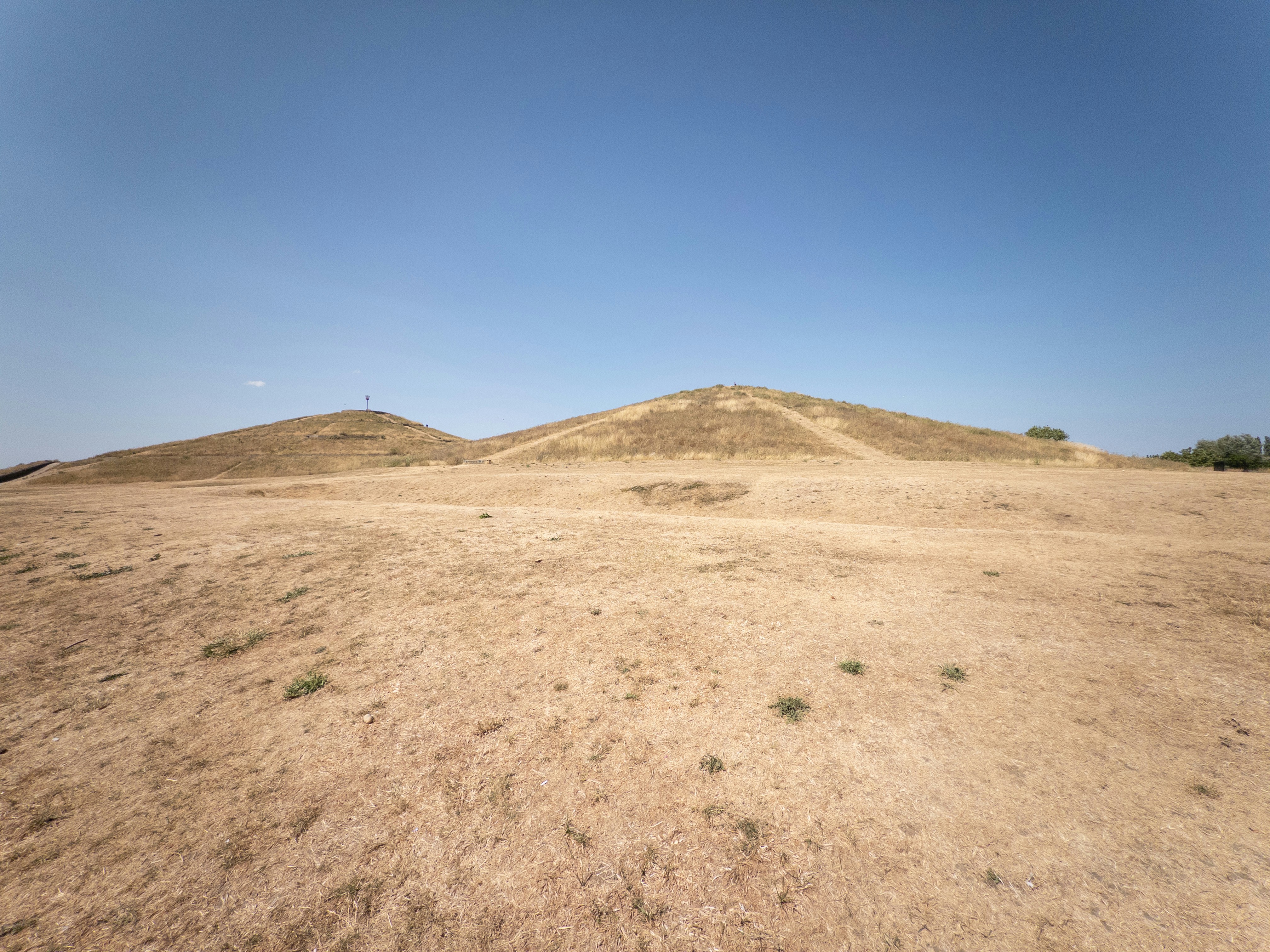 Two dry grassy hills under a clear blue sky in a flat landscape