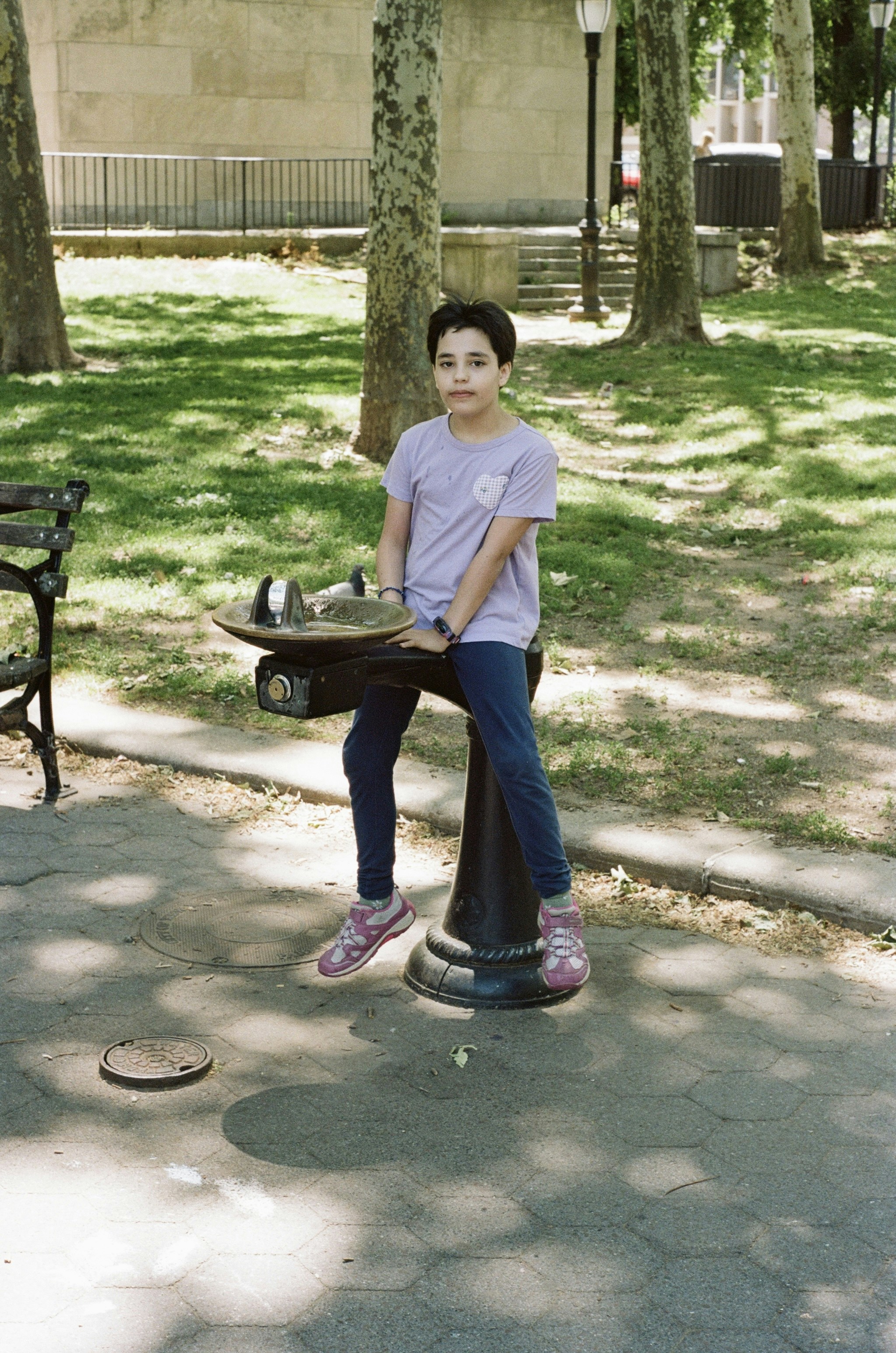 A child in a light purple t-shirt perched on a park water fountain