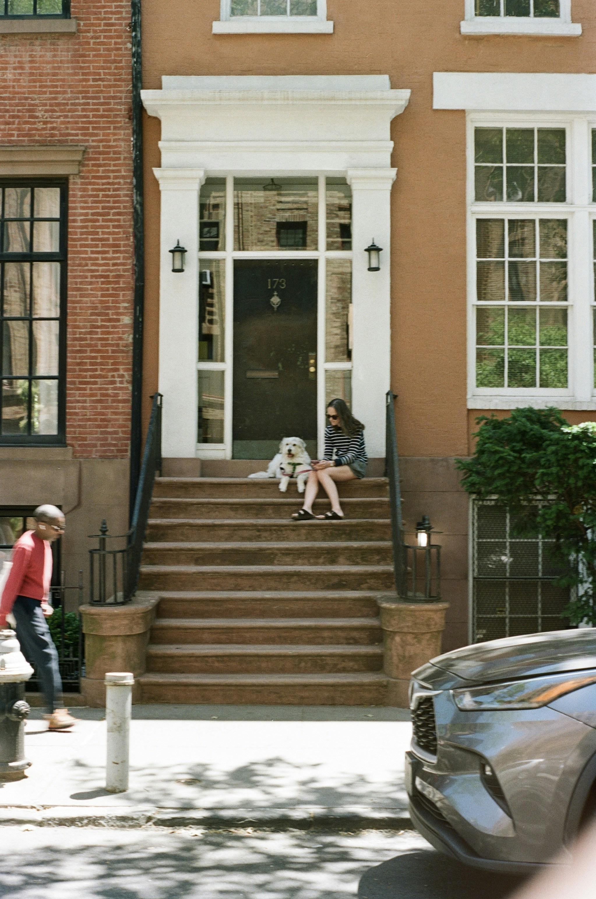 A woman and a white dog on brownstone steps in a city