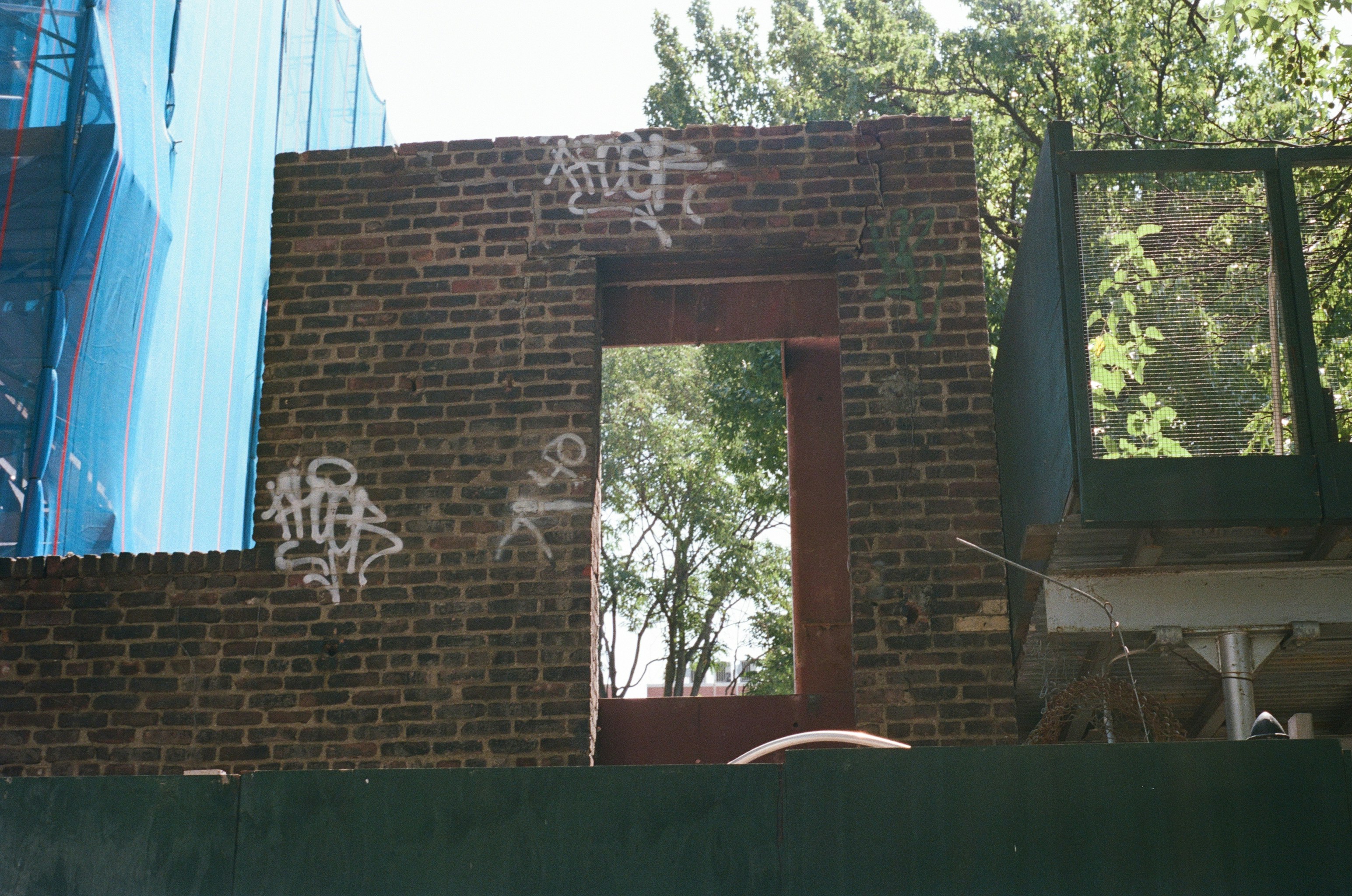 A brick wall with graffiti and a rectangular opening at a construction site