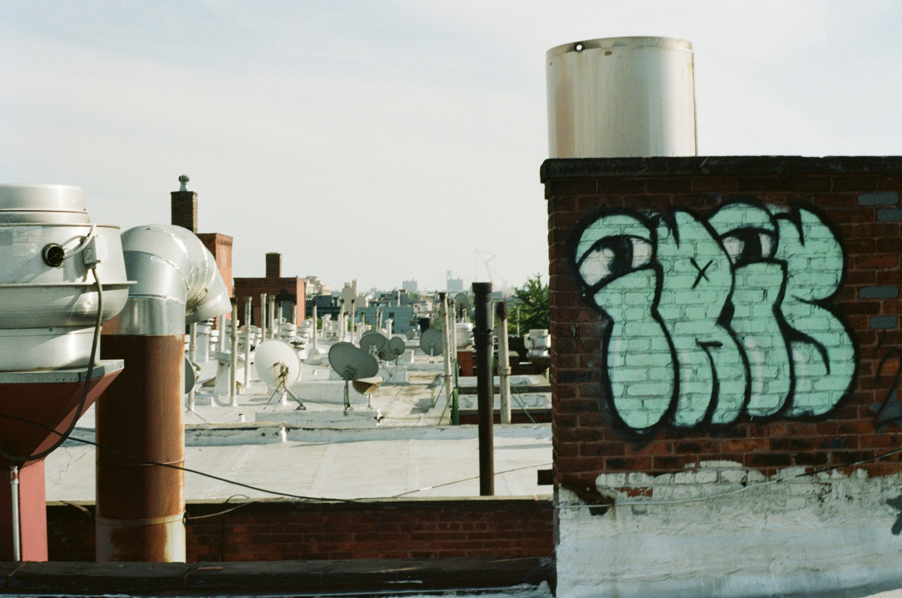 Green graffiti on a brick chimney overlooking a city rooftop with ventilation pipes