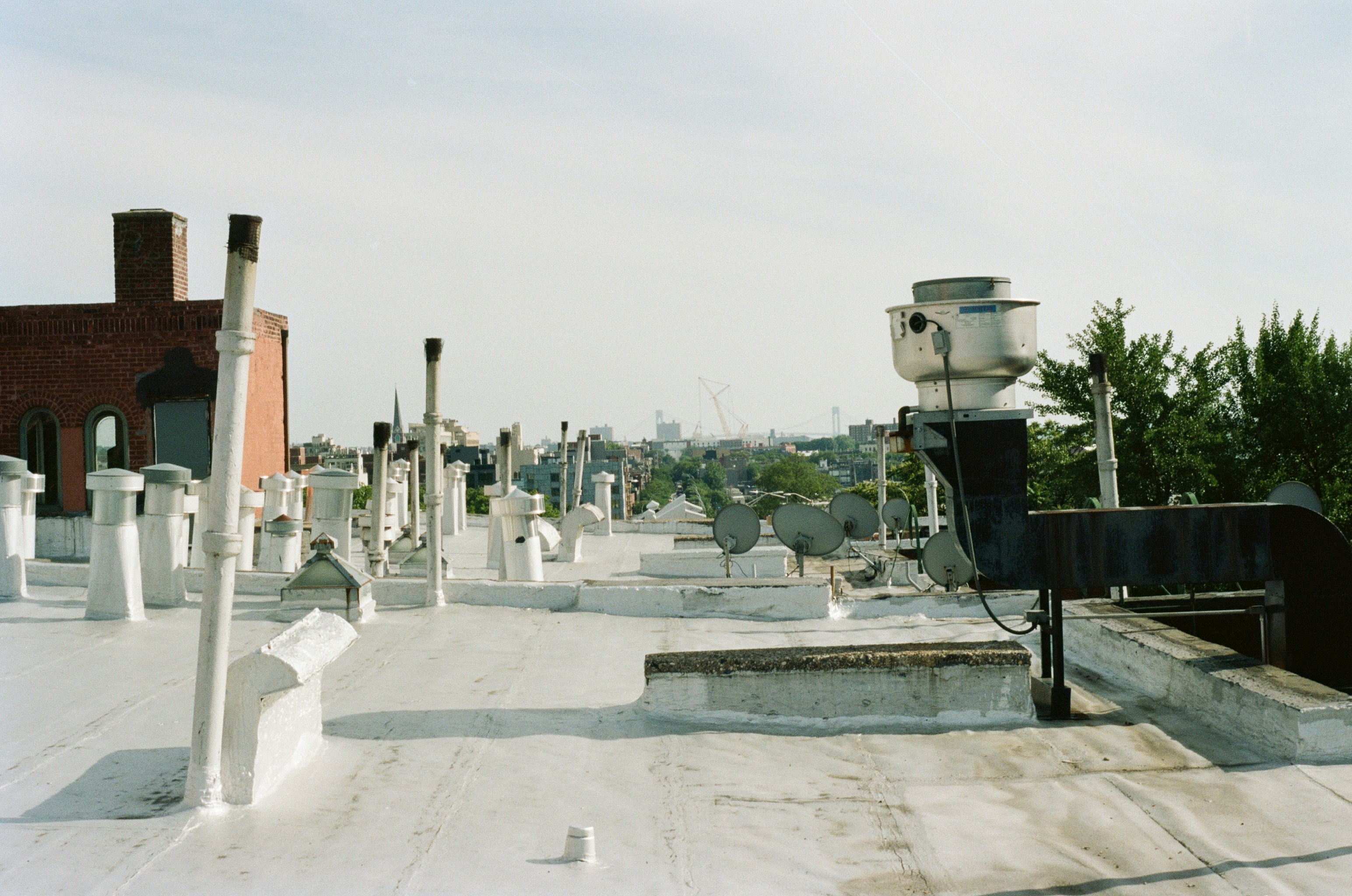 A flat rooftop with numerous white ventilation pipes and a large metal exhaust fan