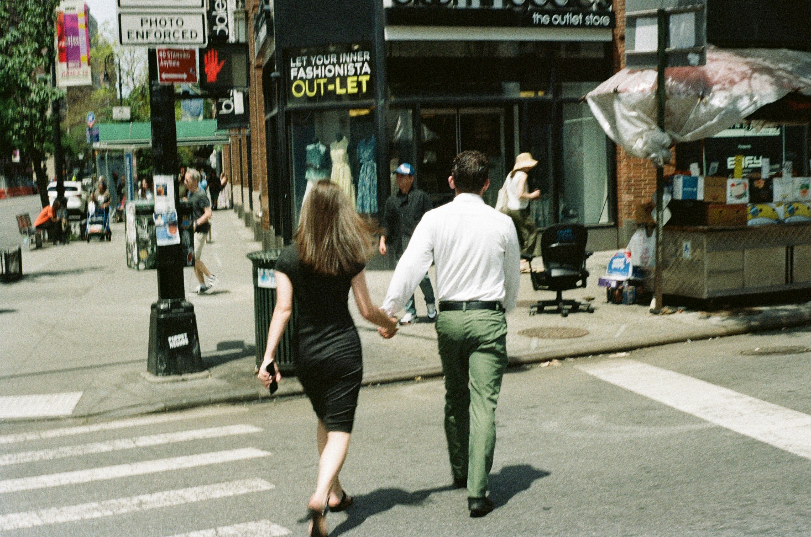 A woman and a man holding hands while crossing a city street