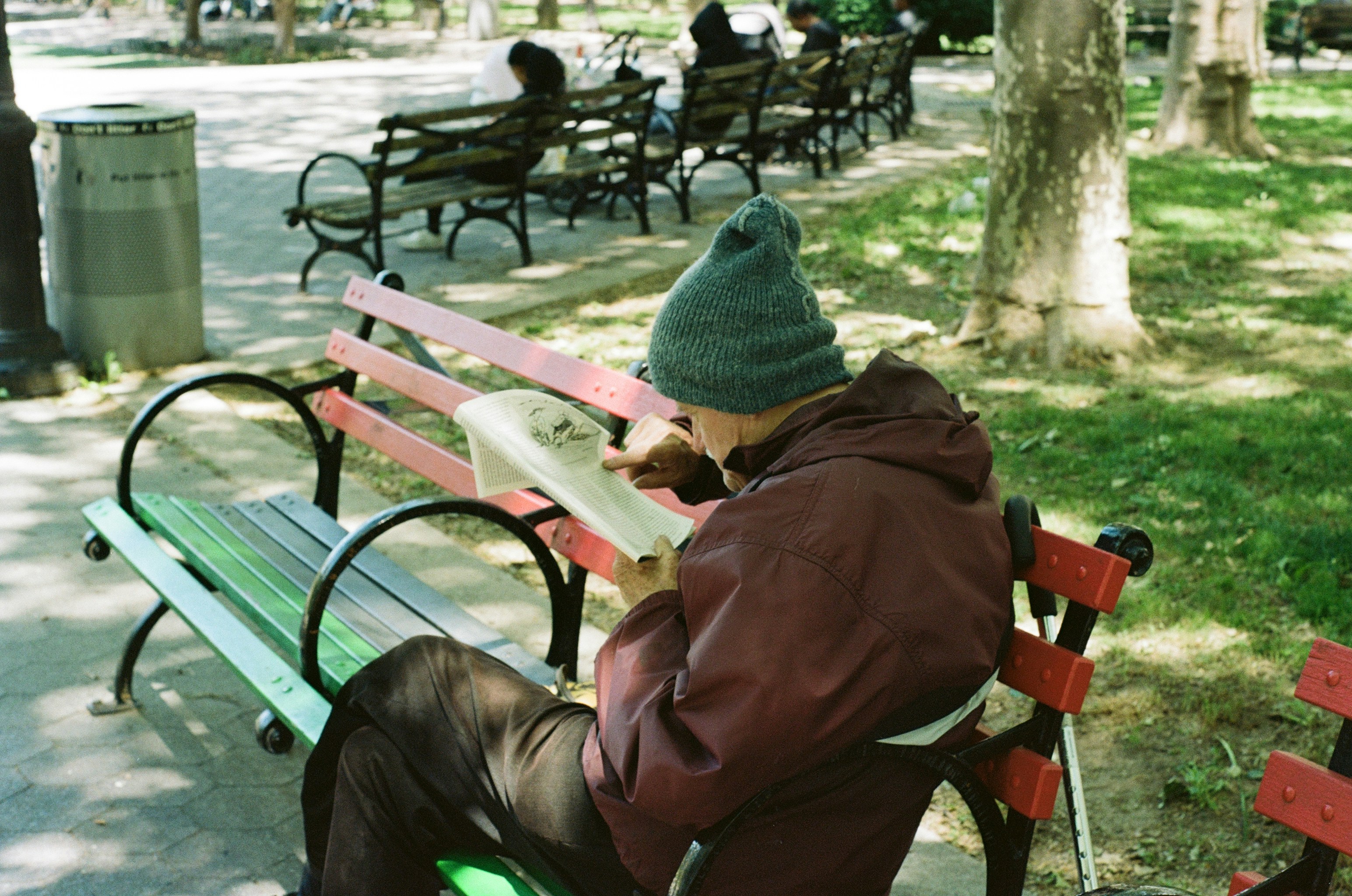An adult in a beanie and jacket reading a book on a park bench