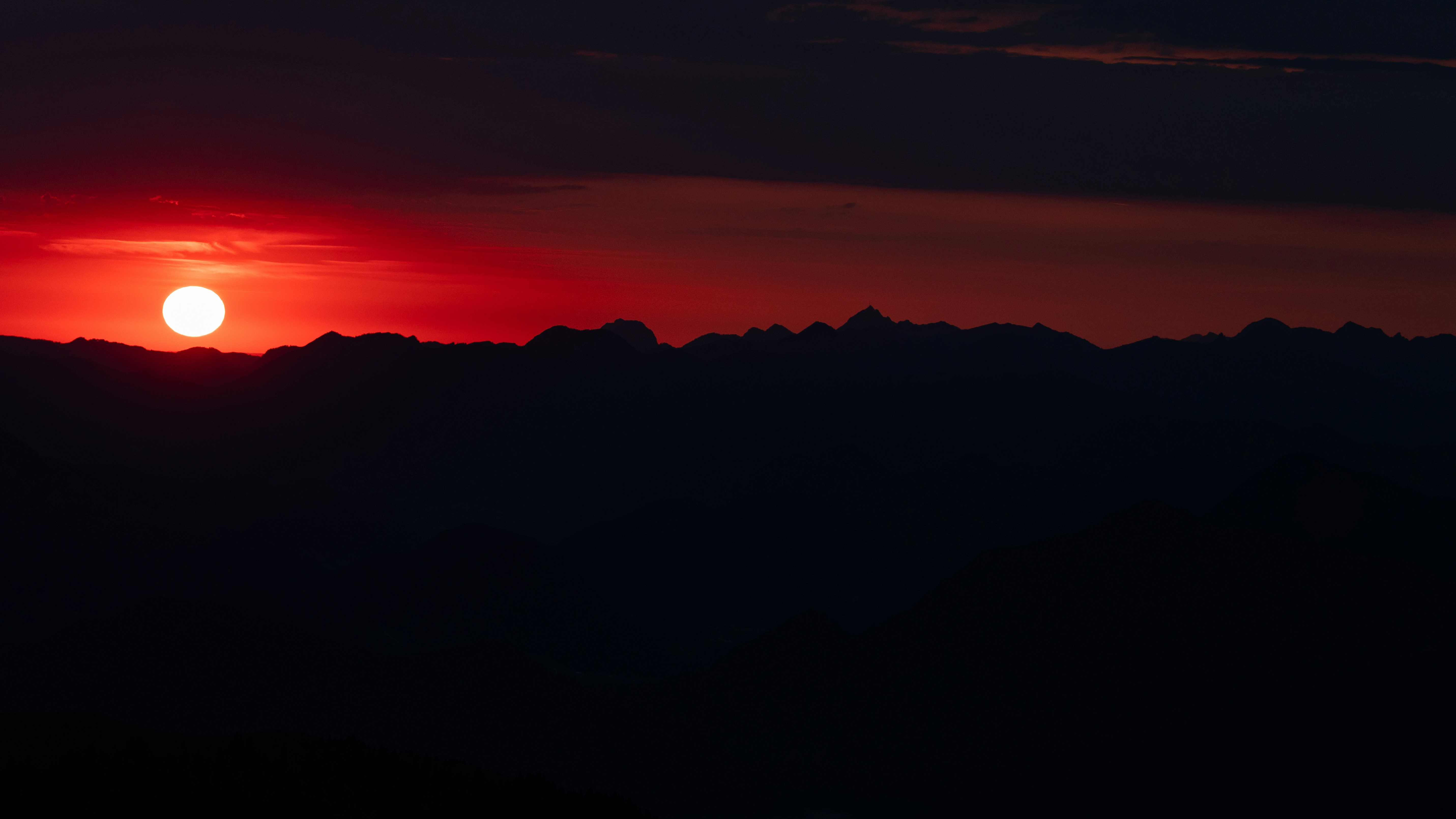 A bright red sun low over dark mountain silhouettes against a deep sky
