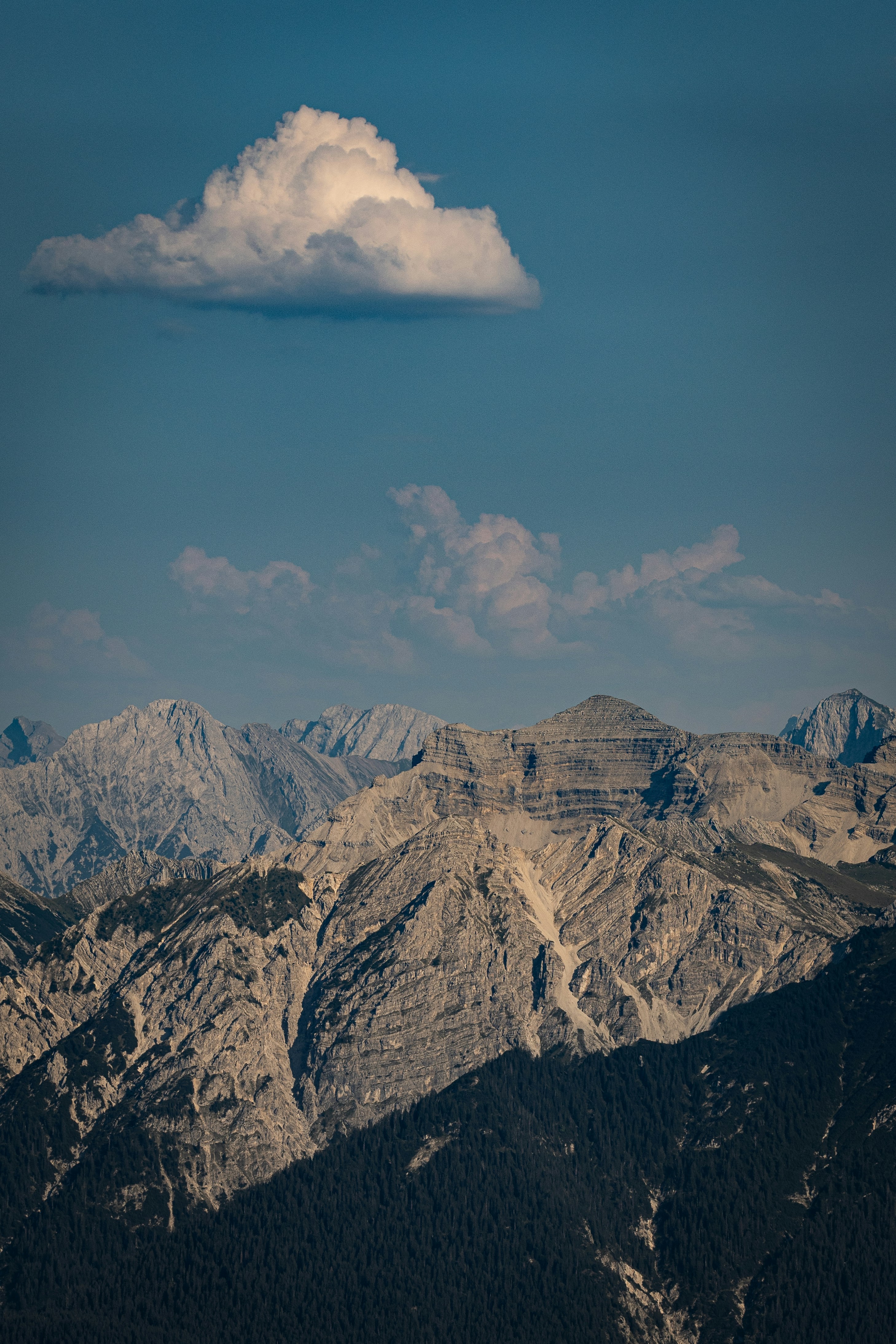 A single white cloud floating above jagged rocky mountain peaks under a blue sky