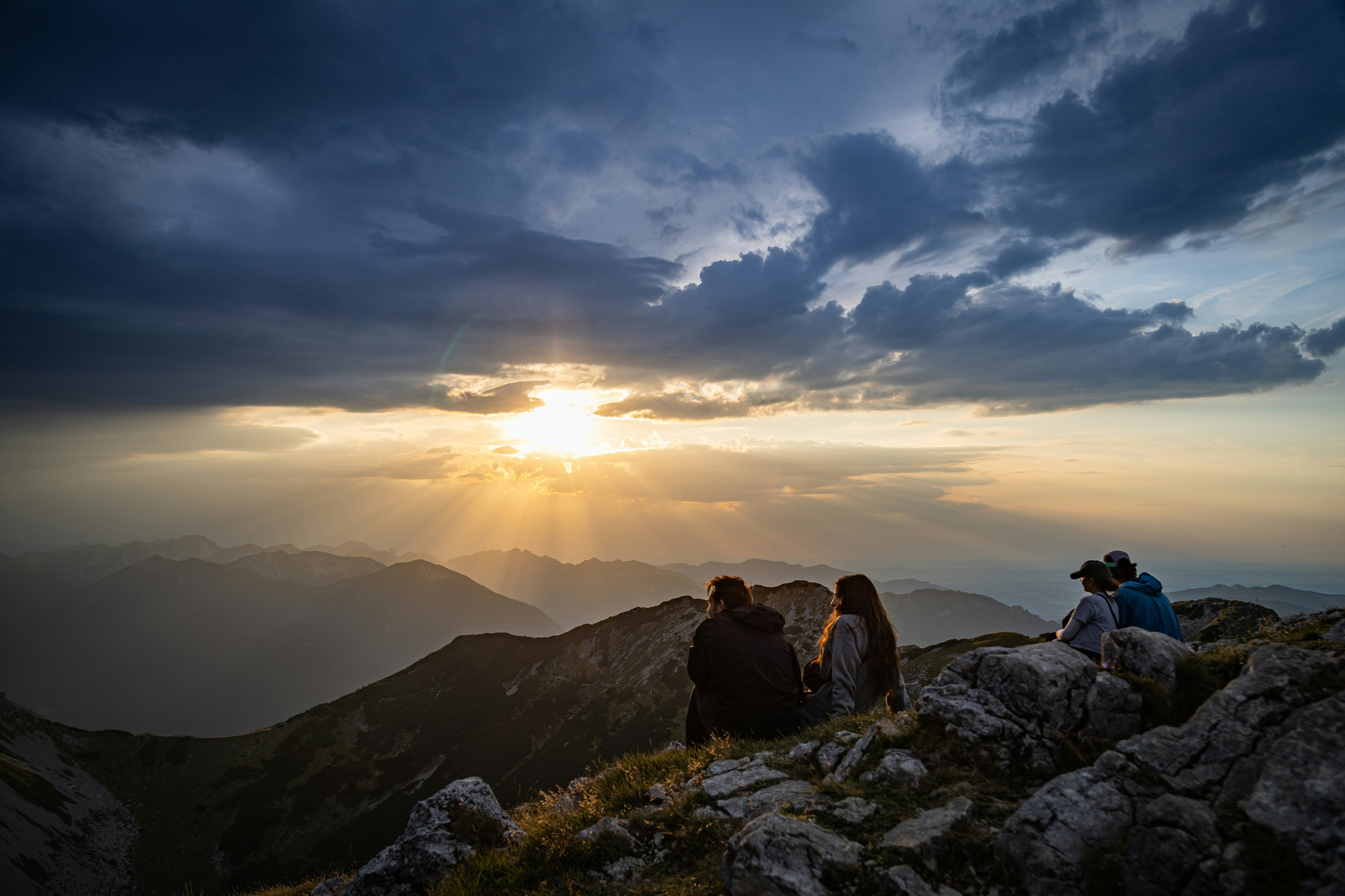 Four people sitting on a rocky mountain ridge watching the low sun