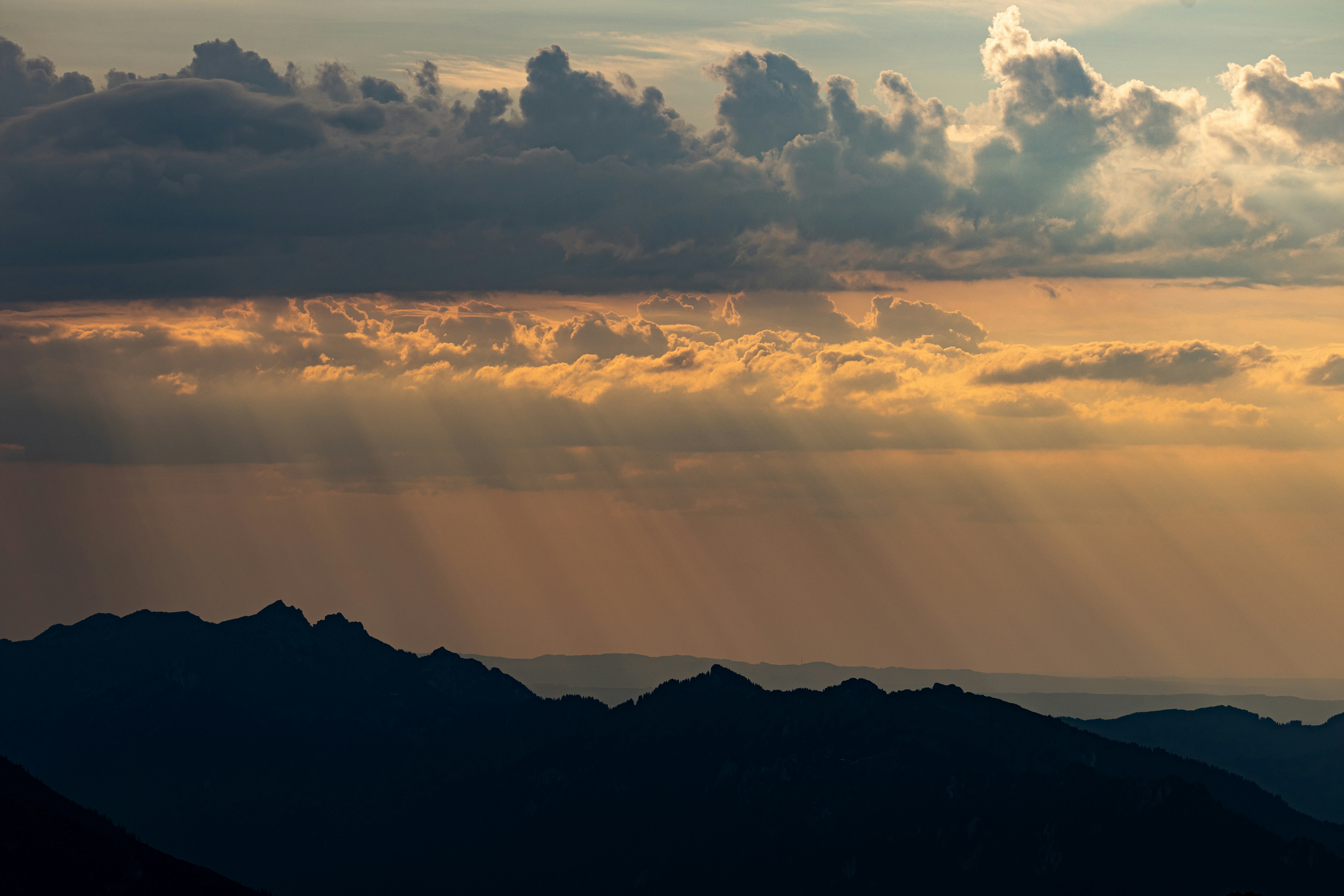 Sunlight rays breaking through clouds over dark mountain silhouettes